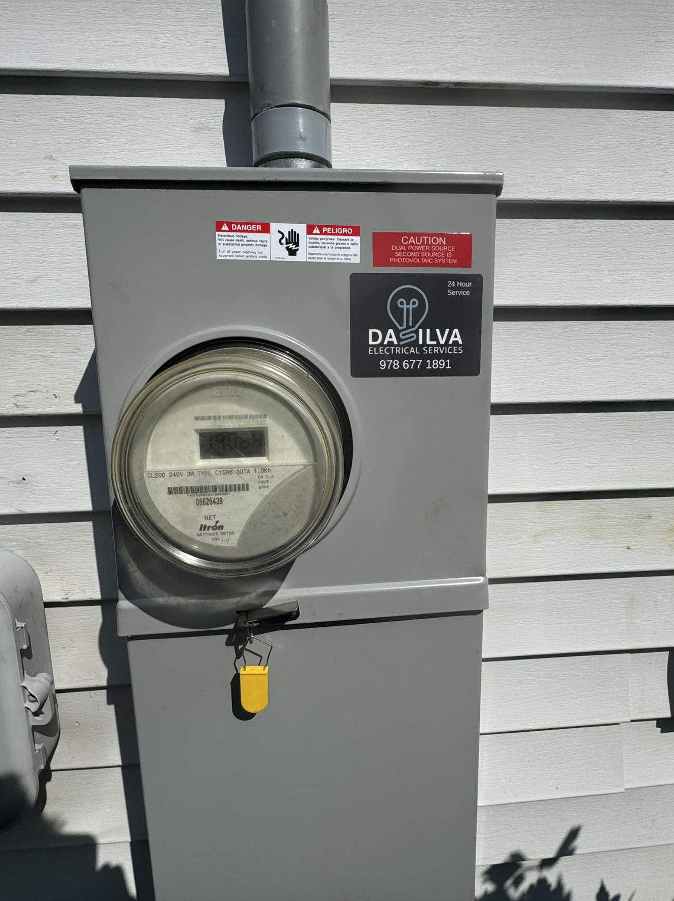 Electric meter box on house exterior with "Da Silva Electrical Services" sticker and safety warnings.