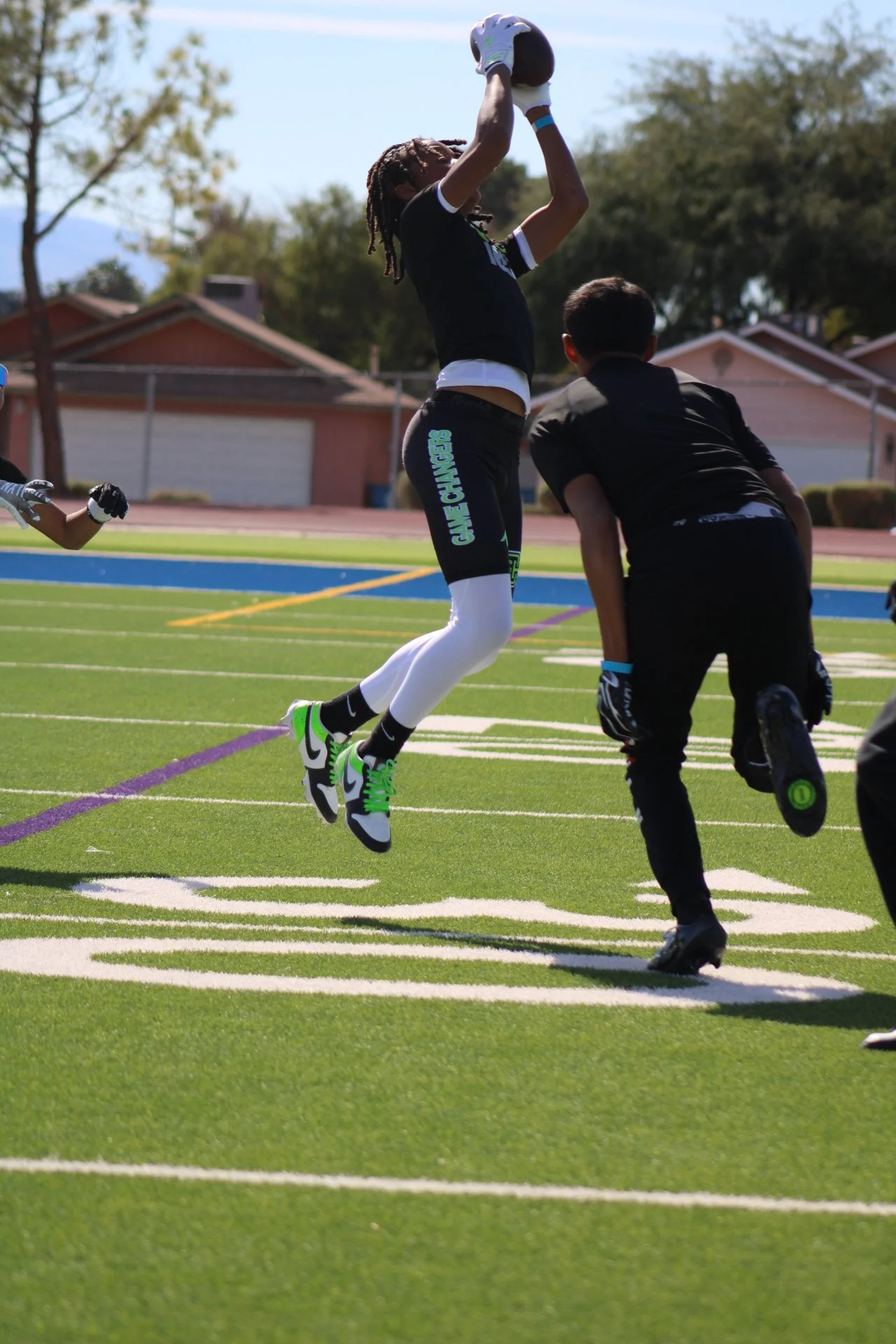 A football player jumping to catch a football during a game on a field, with other players nearby.
