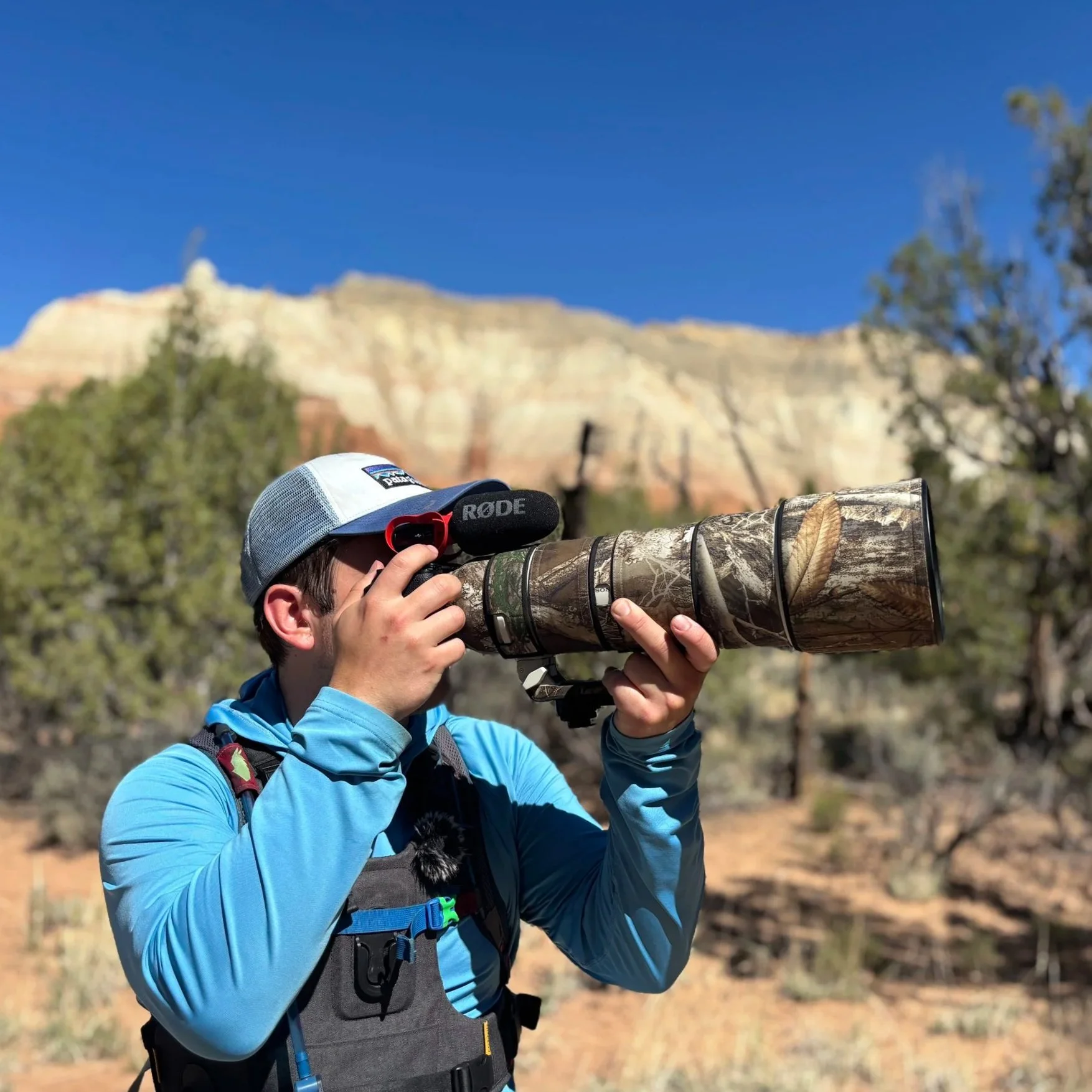 Hawkin holding up his wildlife lens with a desert backdrop featuring cliffs and juniper trees