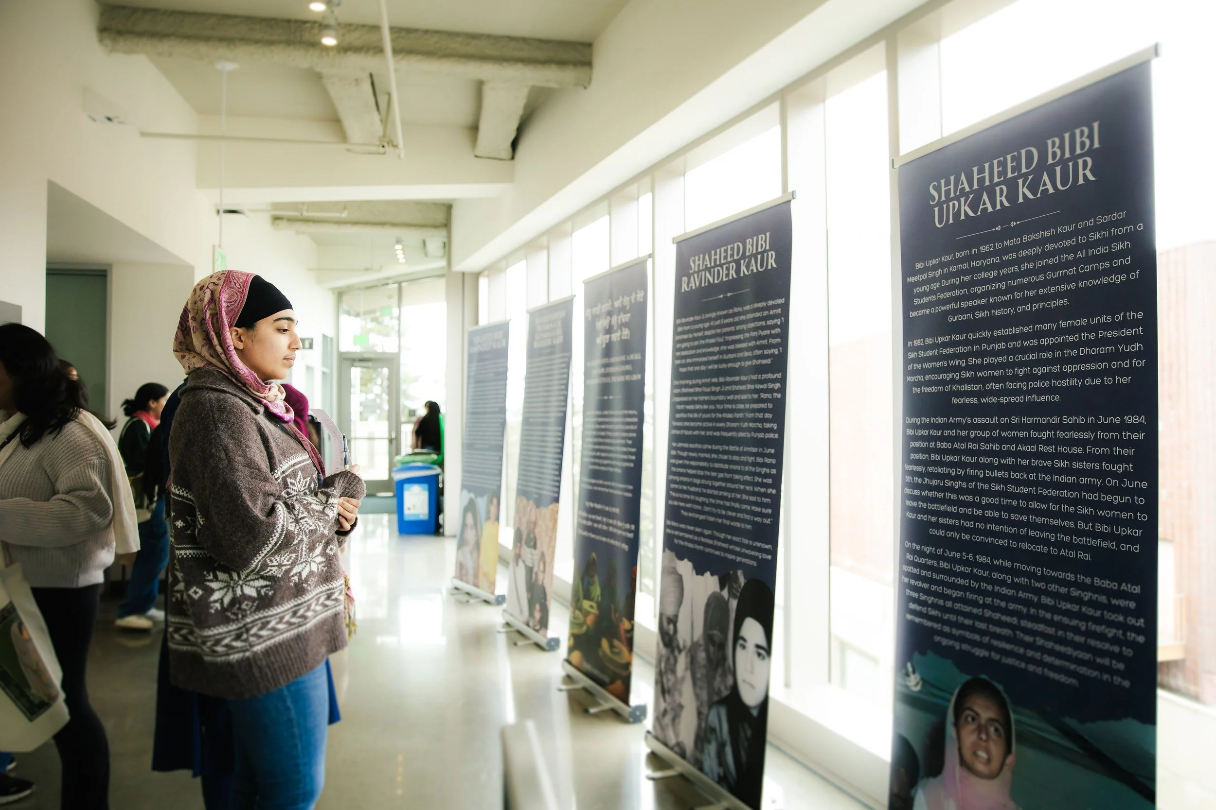 Woman in a winter sweater and headscarf reading informational posters at an indoor exhibition.