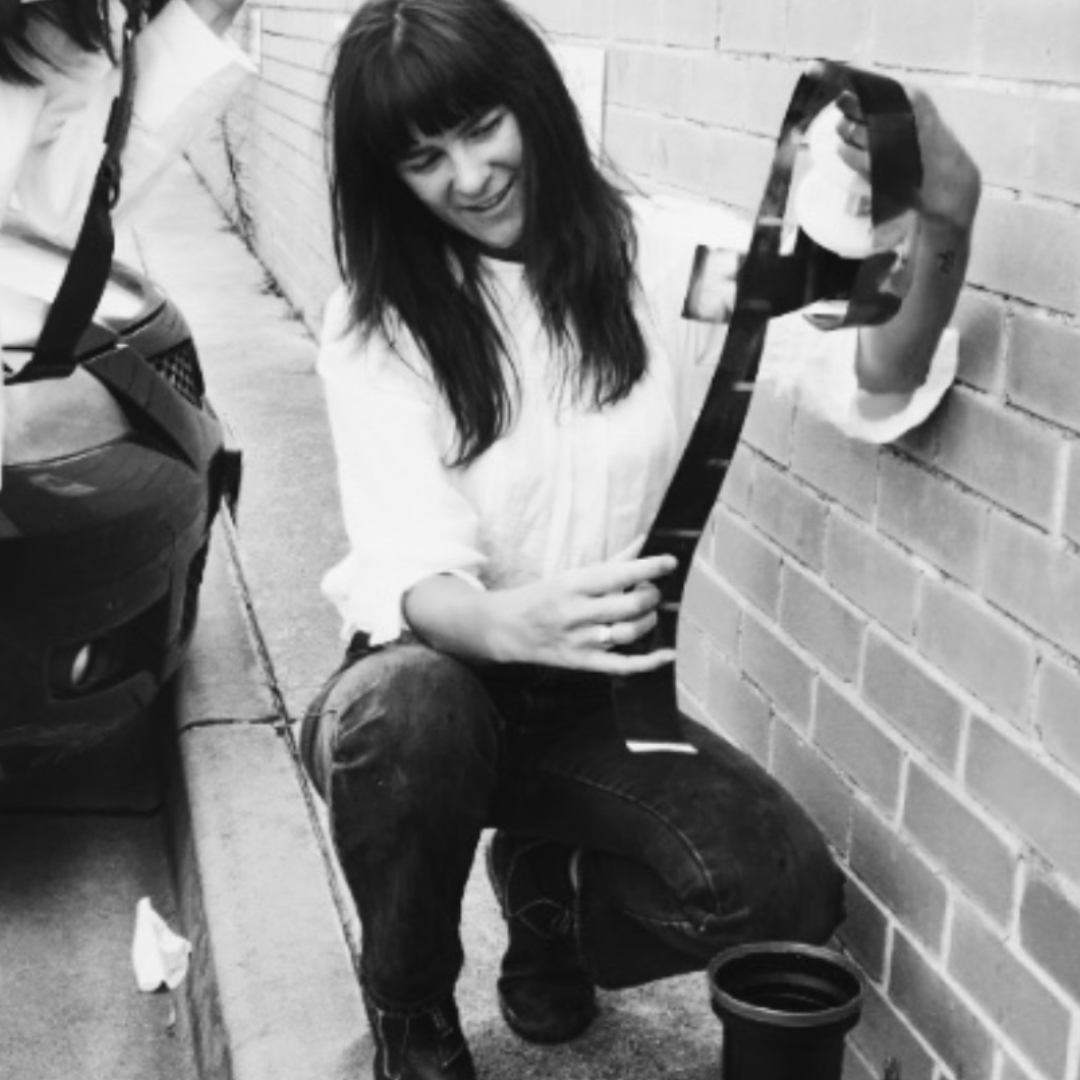 A woman with long dark hair taking a selfie with a smartphone on a brick wall.