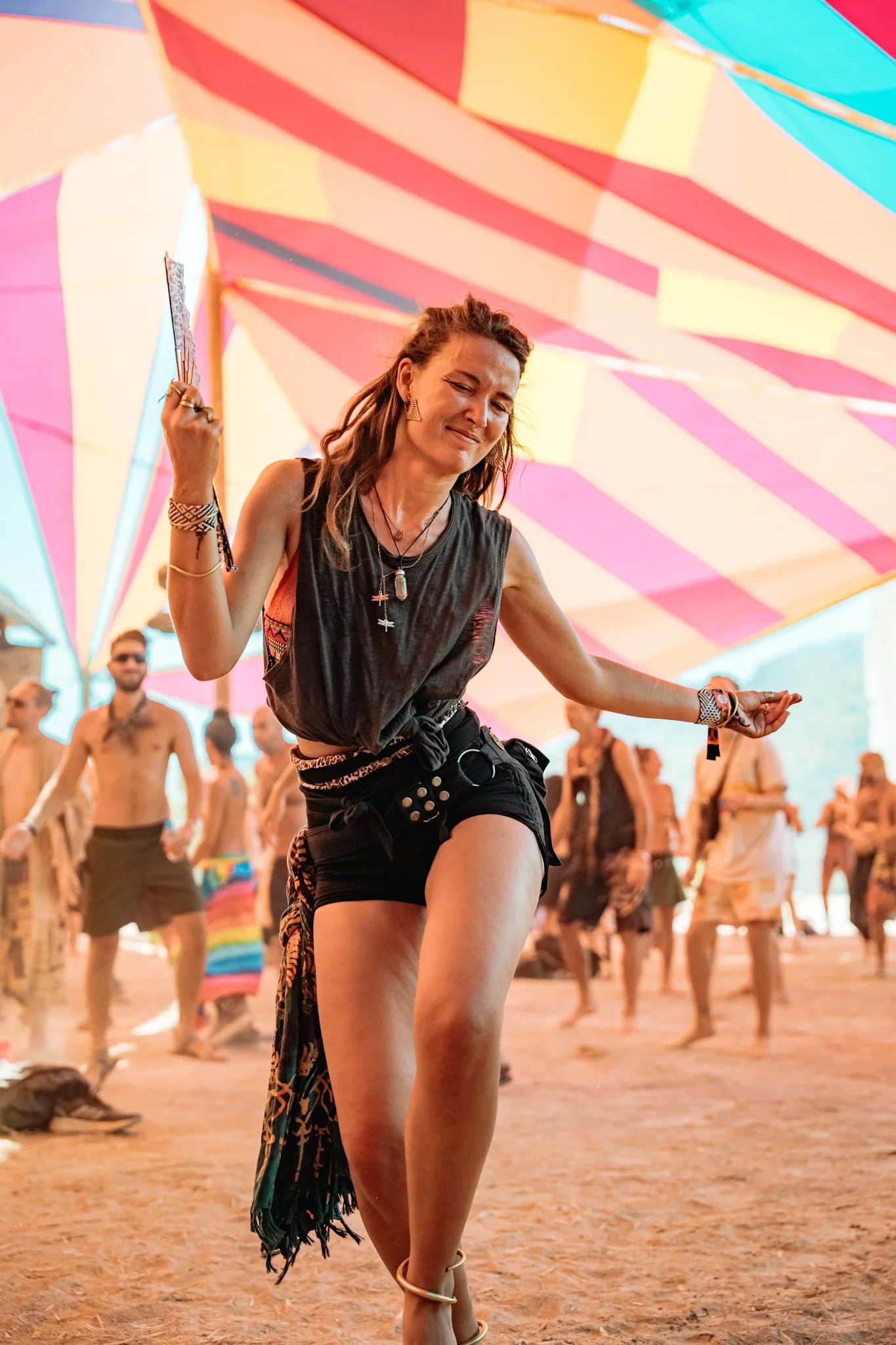 A woman dancing at an outdoor music festival with colorful umbrellas overhead and people in the background.