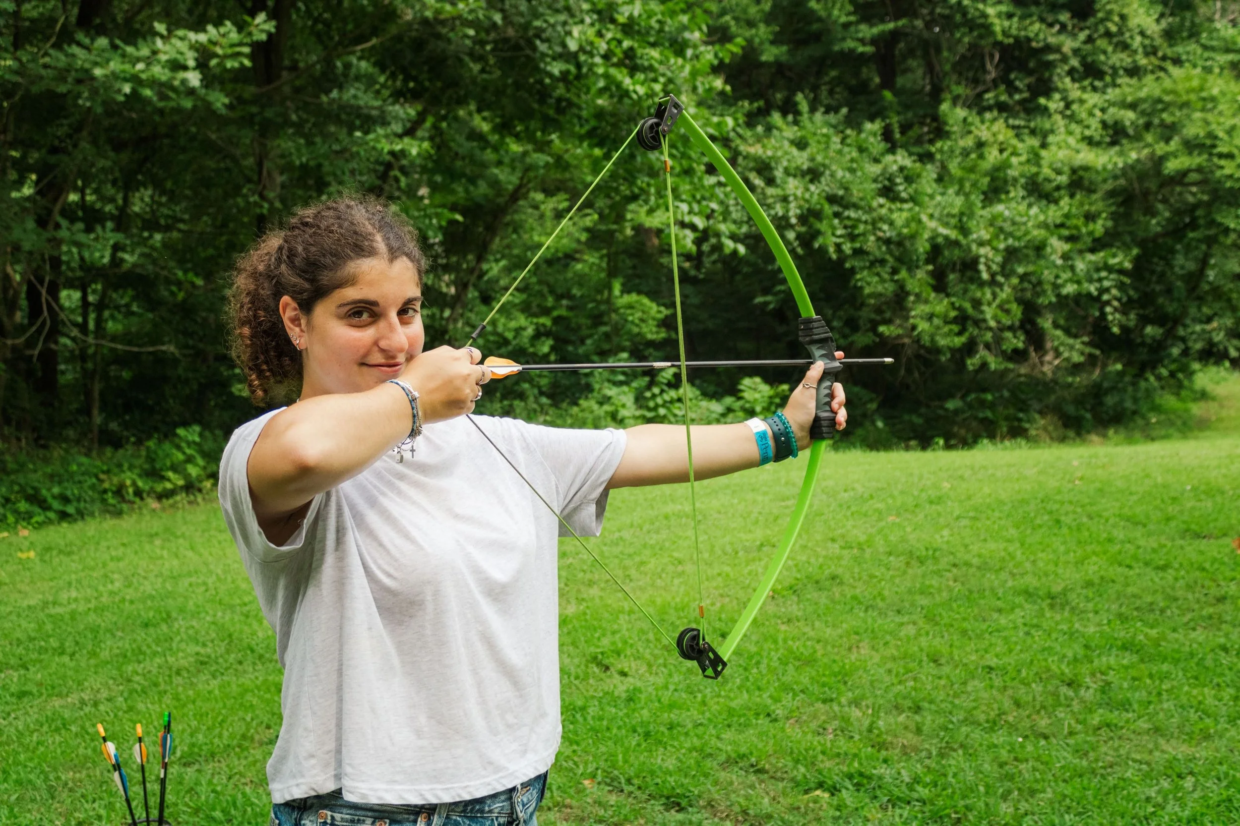 Heartland Christian Camp Paid Gap Year Internship woman standing and smiling with a bow and arrow Outside Near Kansas City, Missouri