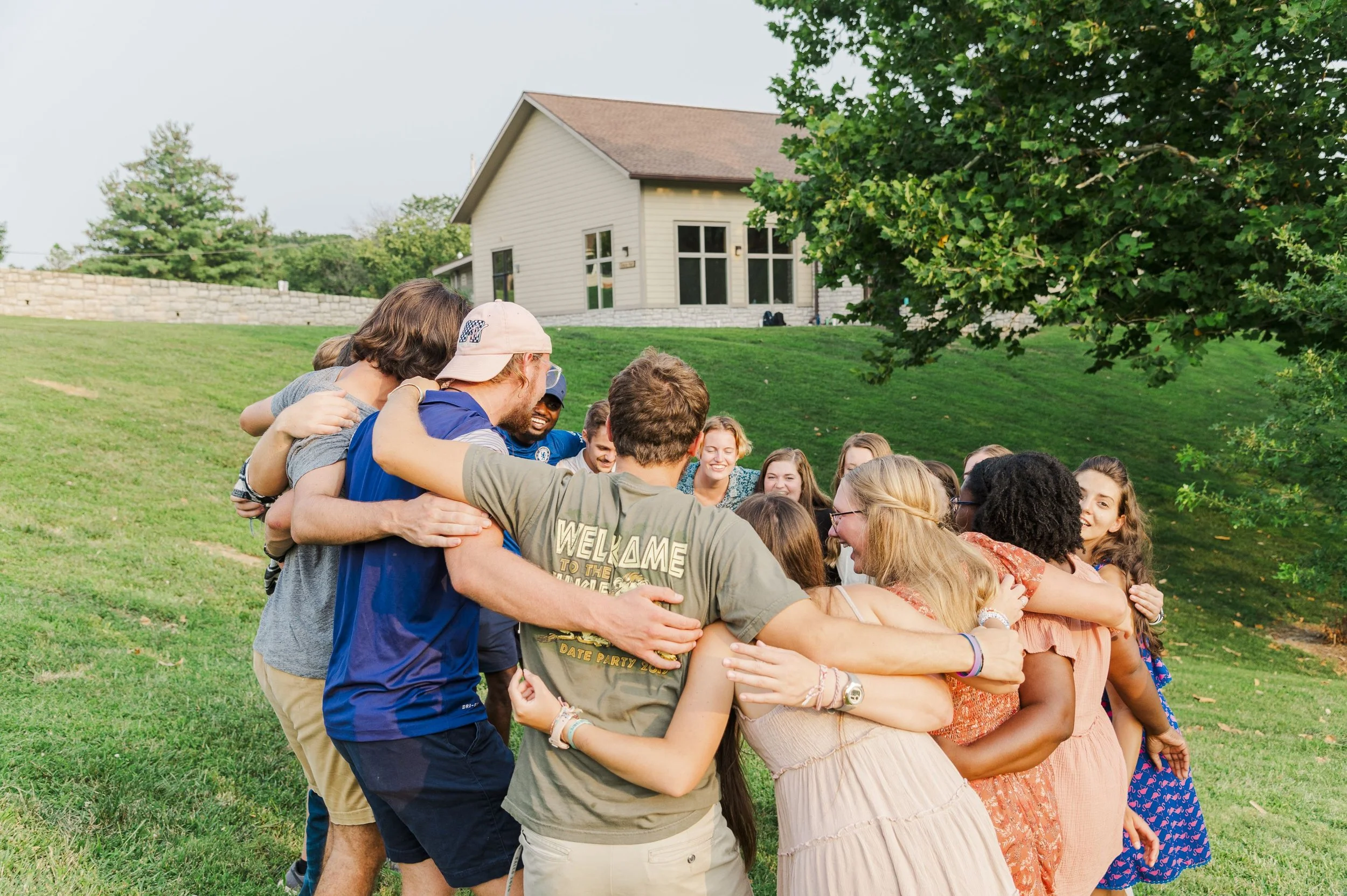 Heartland Christian Camp Paid Gap Year Internship Men and Women standing and smiling with arms linked around one another in a circle Outside Near Kansas City, Missouri