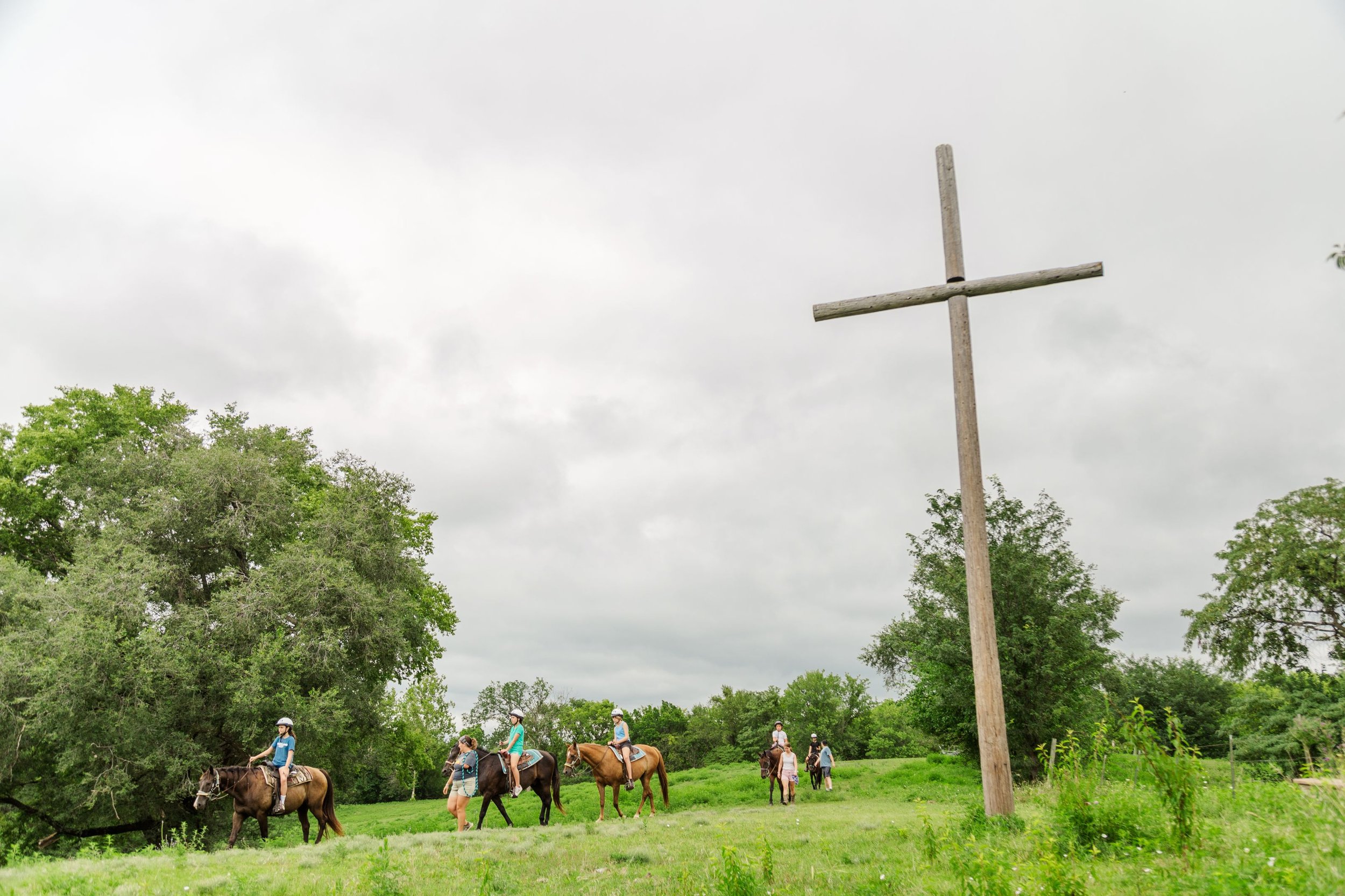 Heartland Christian Camp Paid Gap Year Internship Men and Women riding horses around a cross Together Outside Near Kansas City, Missouri