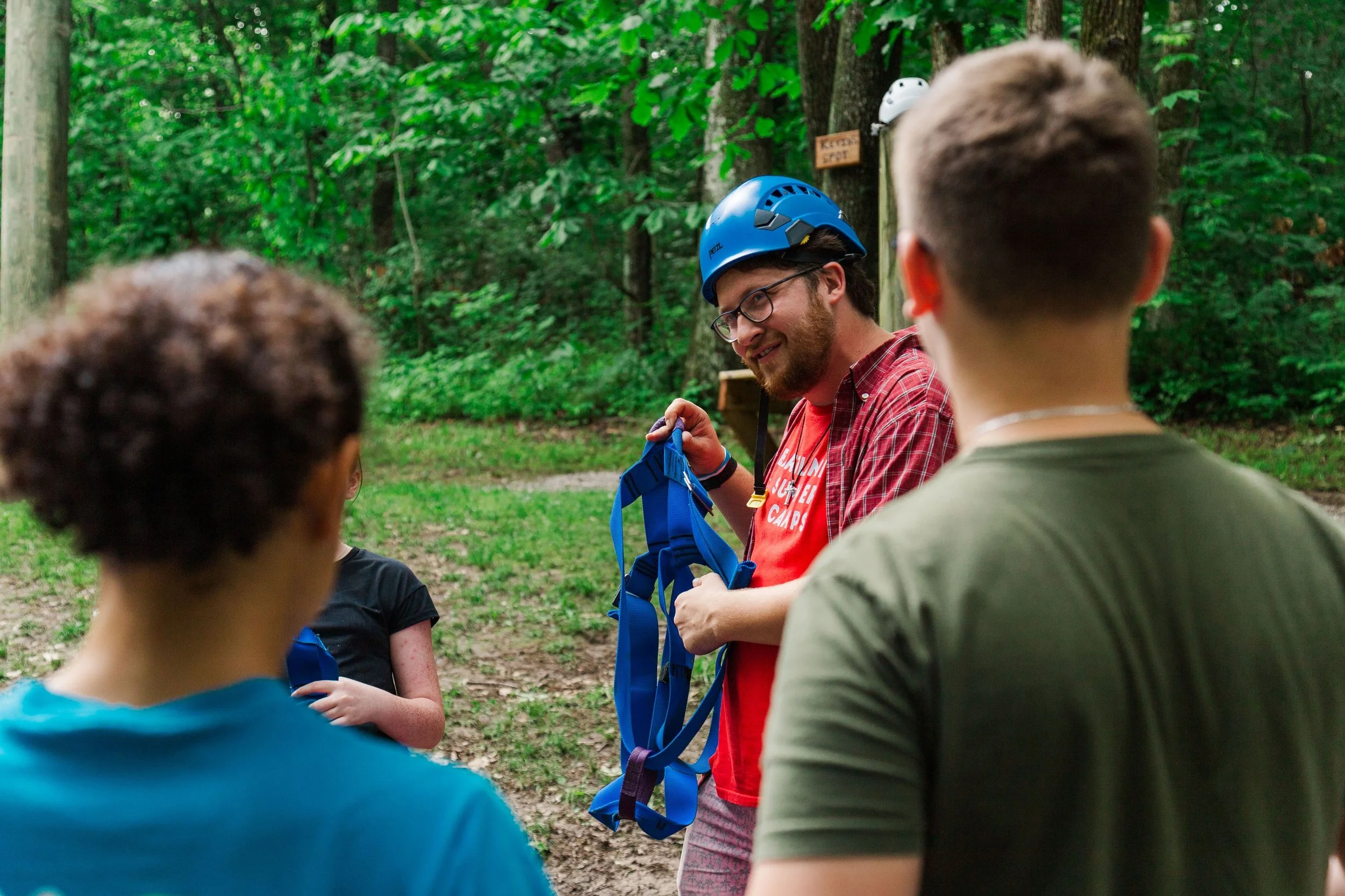 Heartland Christian Camp Paid Gap Year Internship Men and Women Standing and listening to challenge course director with climbing harness Outside Near Kansas City, Missouri