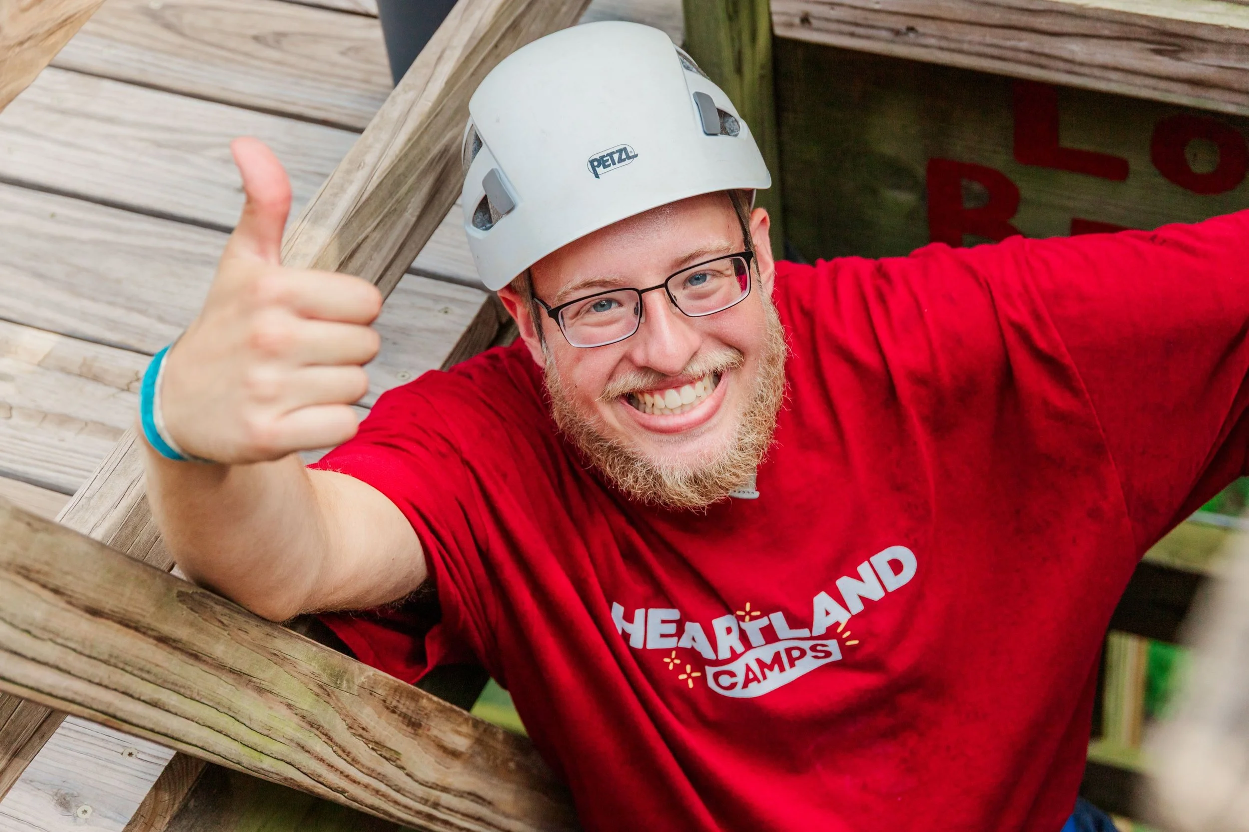 Heartland Christian Camp Paid Gap Year Internship man standing and smiling while wearing a helmet and harness on a high ropes course Outside Near Kansas City, Missouri