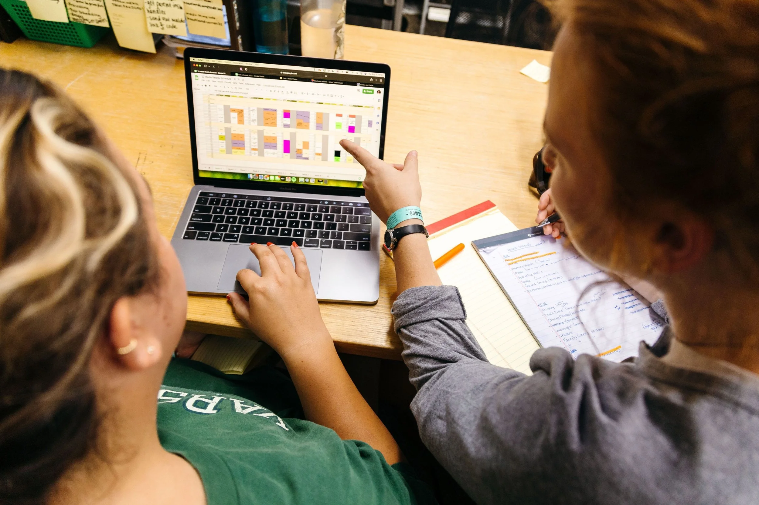 Heartland Christian Camp Paid Gap Year Internship women working in an office on a computer together and pointing at details on their project near Kansas City, Missouri