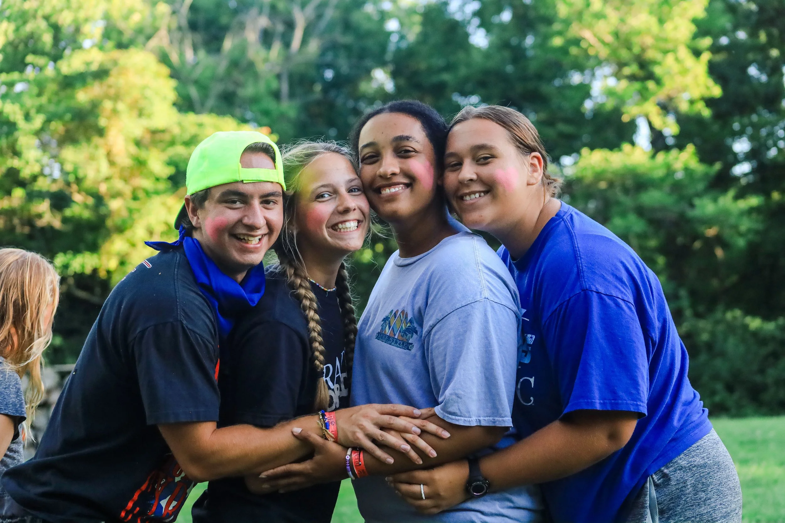 Four smiling college students in Heartland's Christian Gap Year program dressed in casual clothing embracing outdoors with green trees in the background.