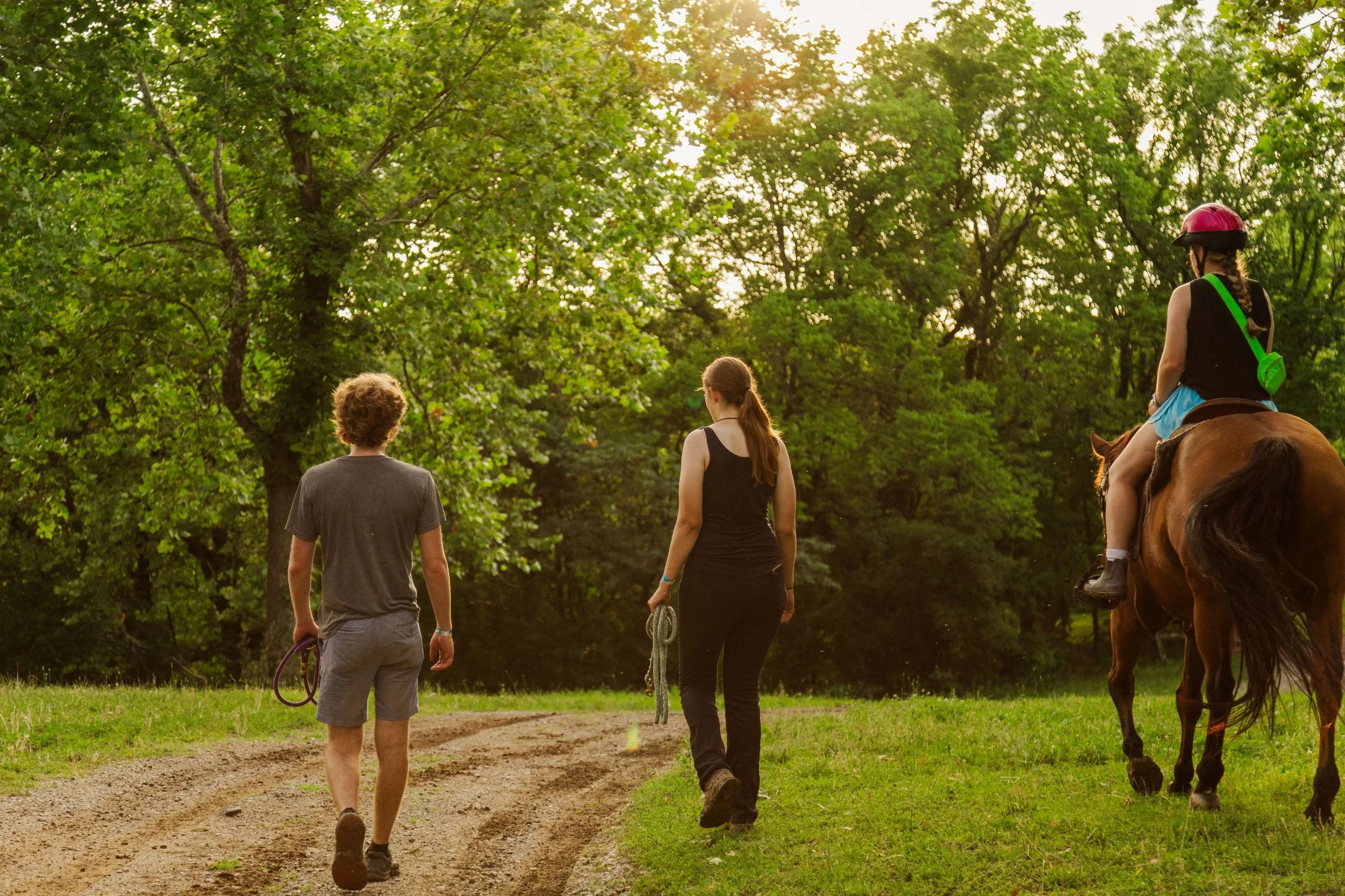 Heartland Christian Camp Paid Gap Year Internship Men and Women walking on a trail near a forest and one is riding a horse Outside Near Kansas City, Missouri