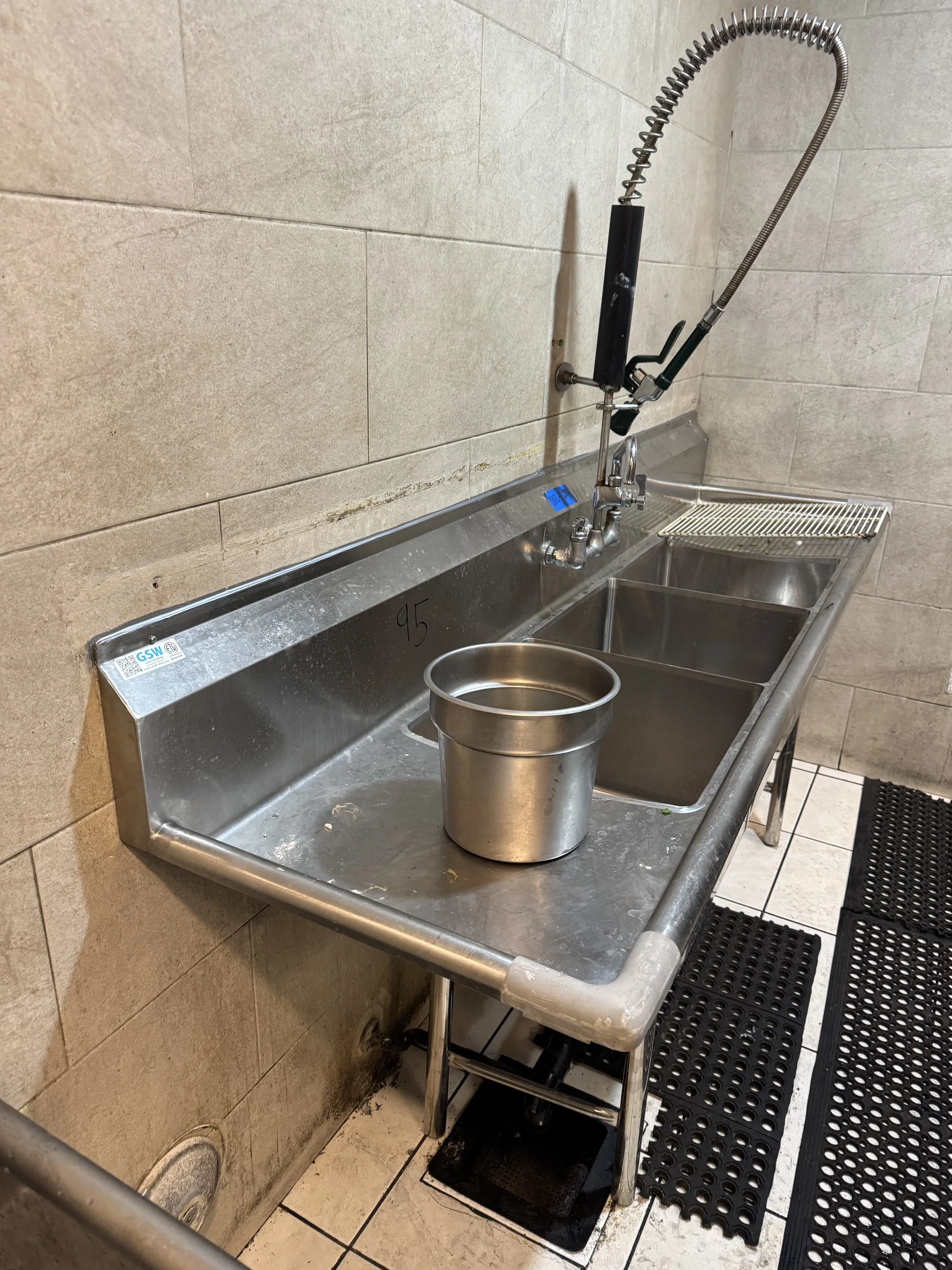 Stainless steel commercial kitchen sink with three basins, a bucket in the middle, and a high-arc faucet with a sprayer head.