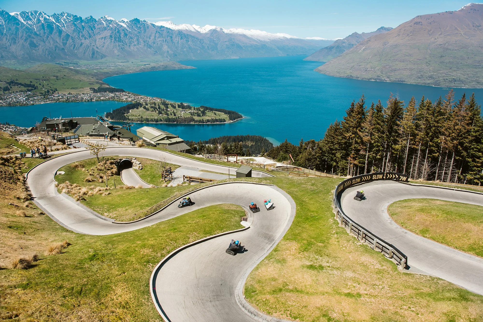A scenic mountain road with sharp turns, overlooking a large lake surrounded by mountains and forest.