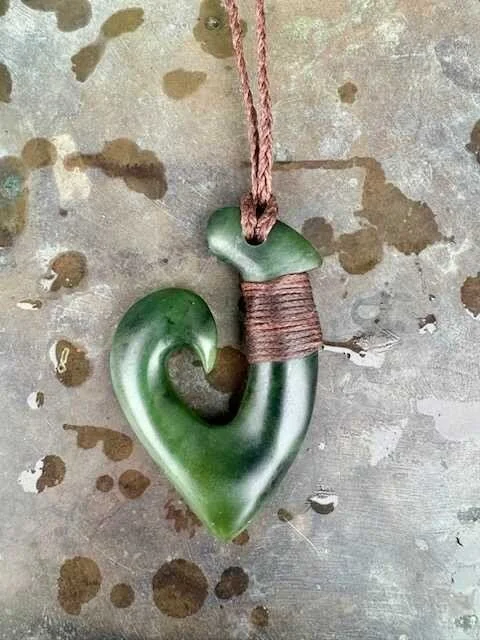 A green carved jade pendant shaped like a question mark with a wrapped top, hanging from a pink string.