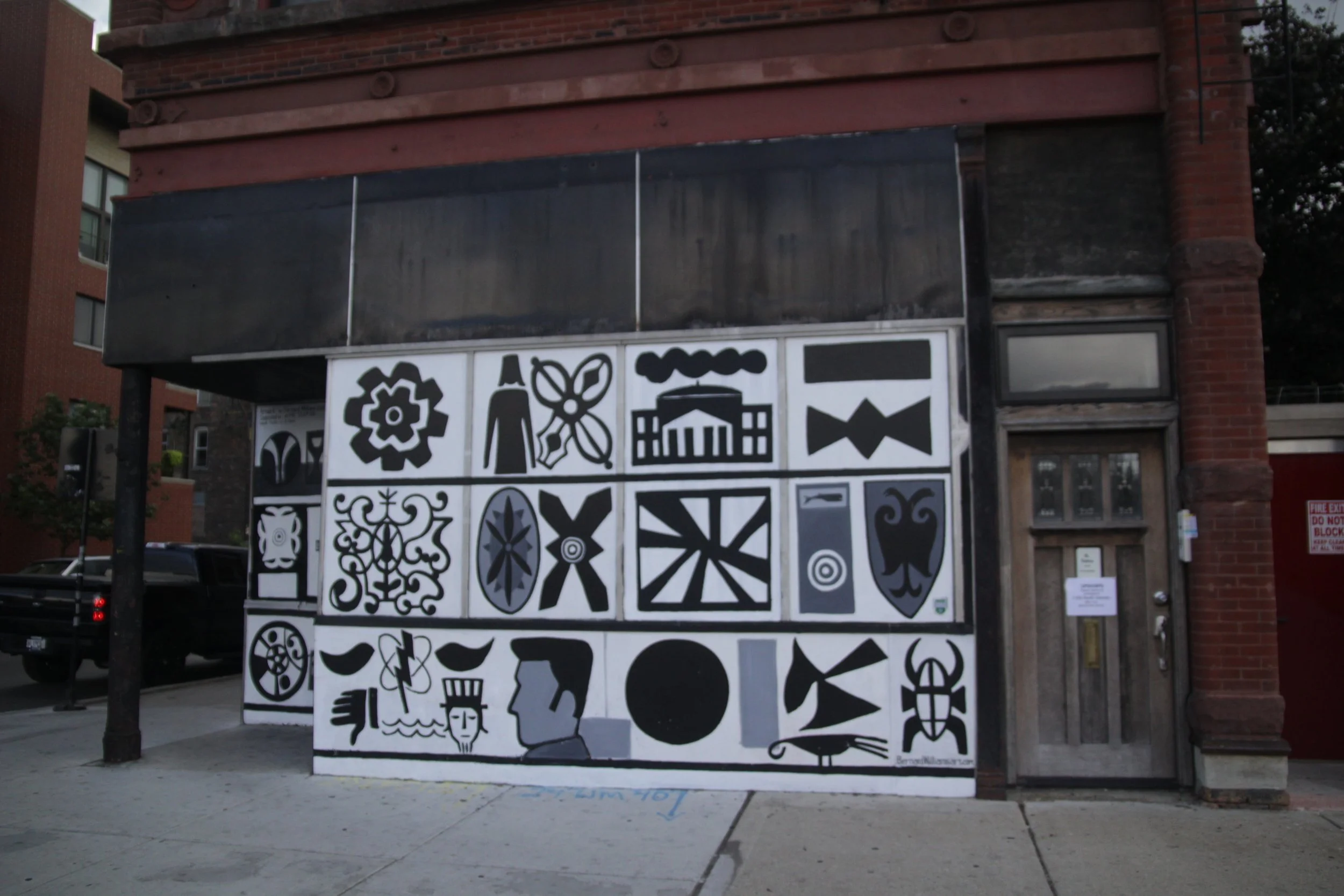 Street mural featuring various black and white abstract designs and symbols on a building facade.