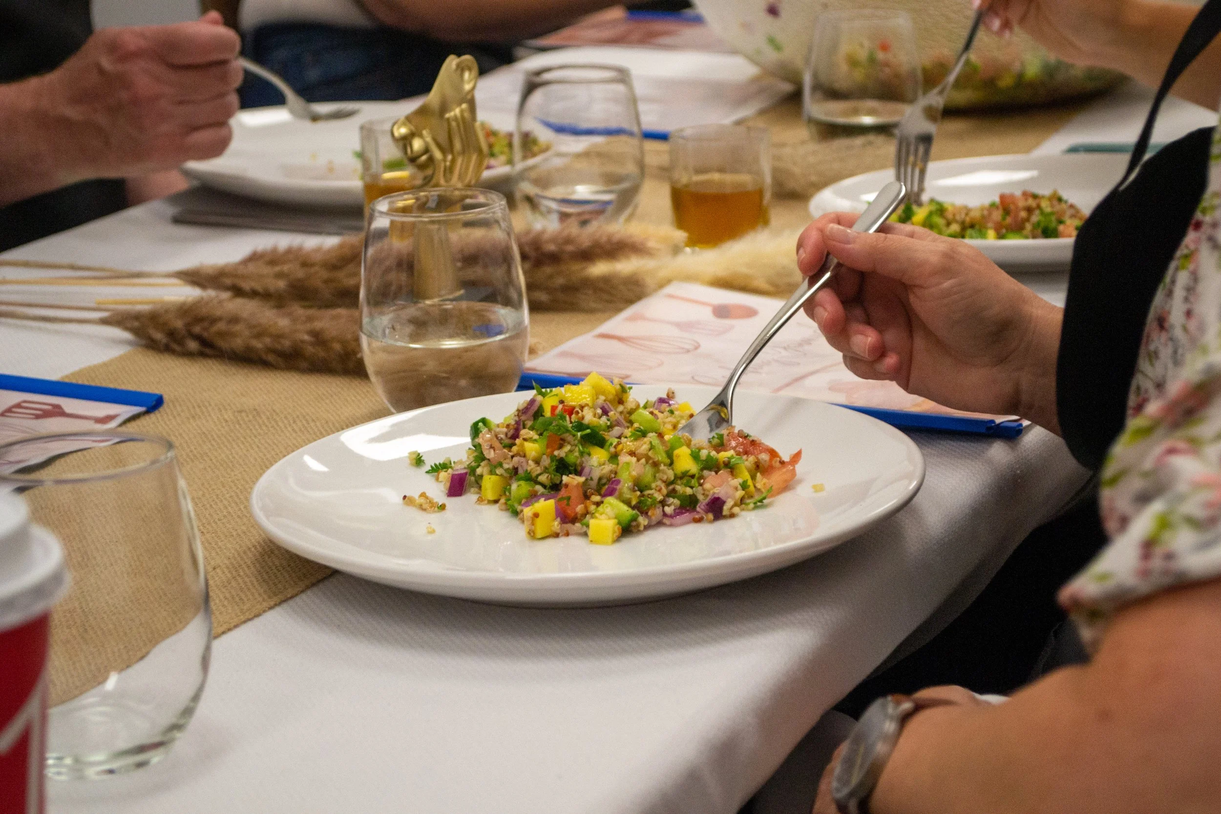 People eating a colorful salad at a dining table with glasses of drinks and plates of food.