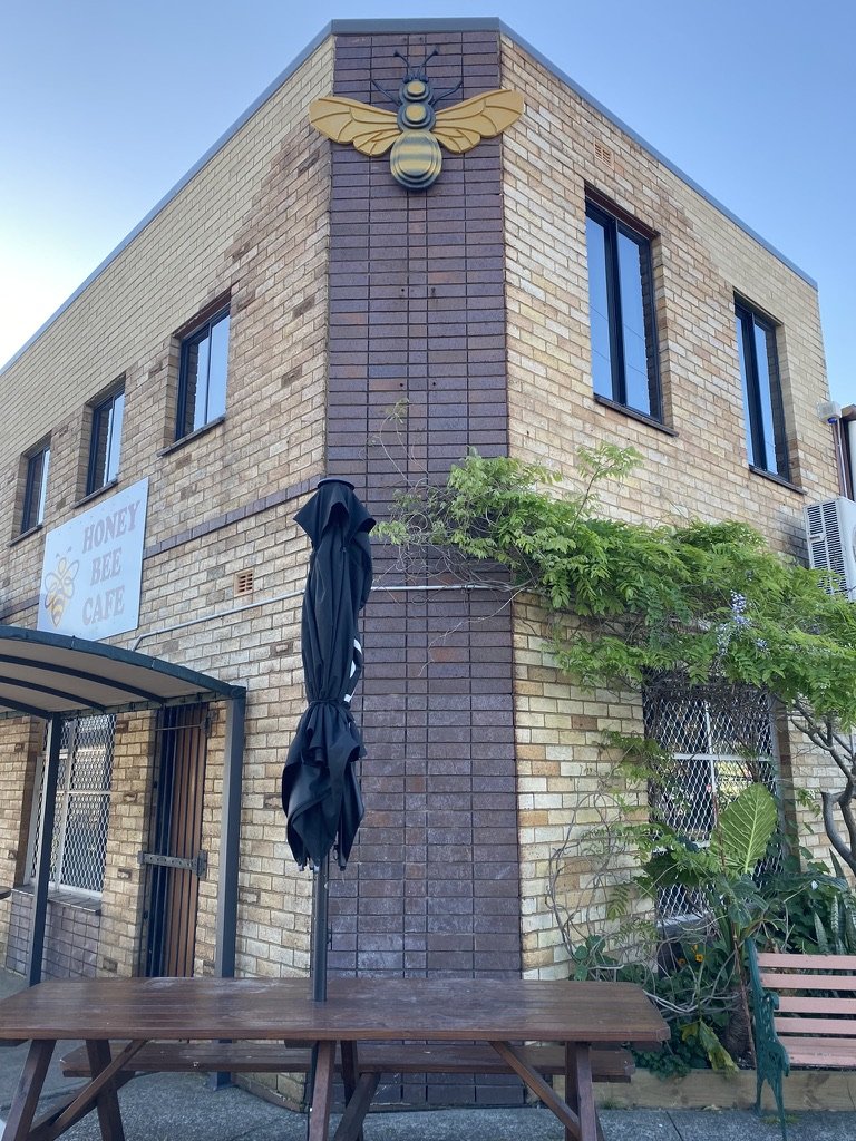 Custom Honey Bee Café signage with large bee sculpture mounted on a brick building exterior.