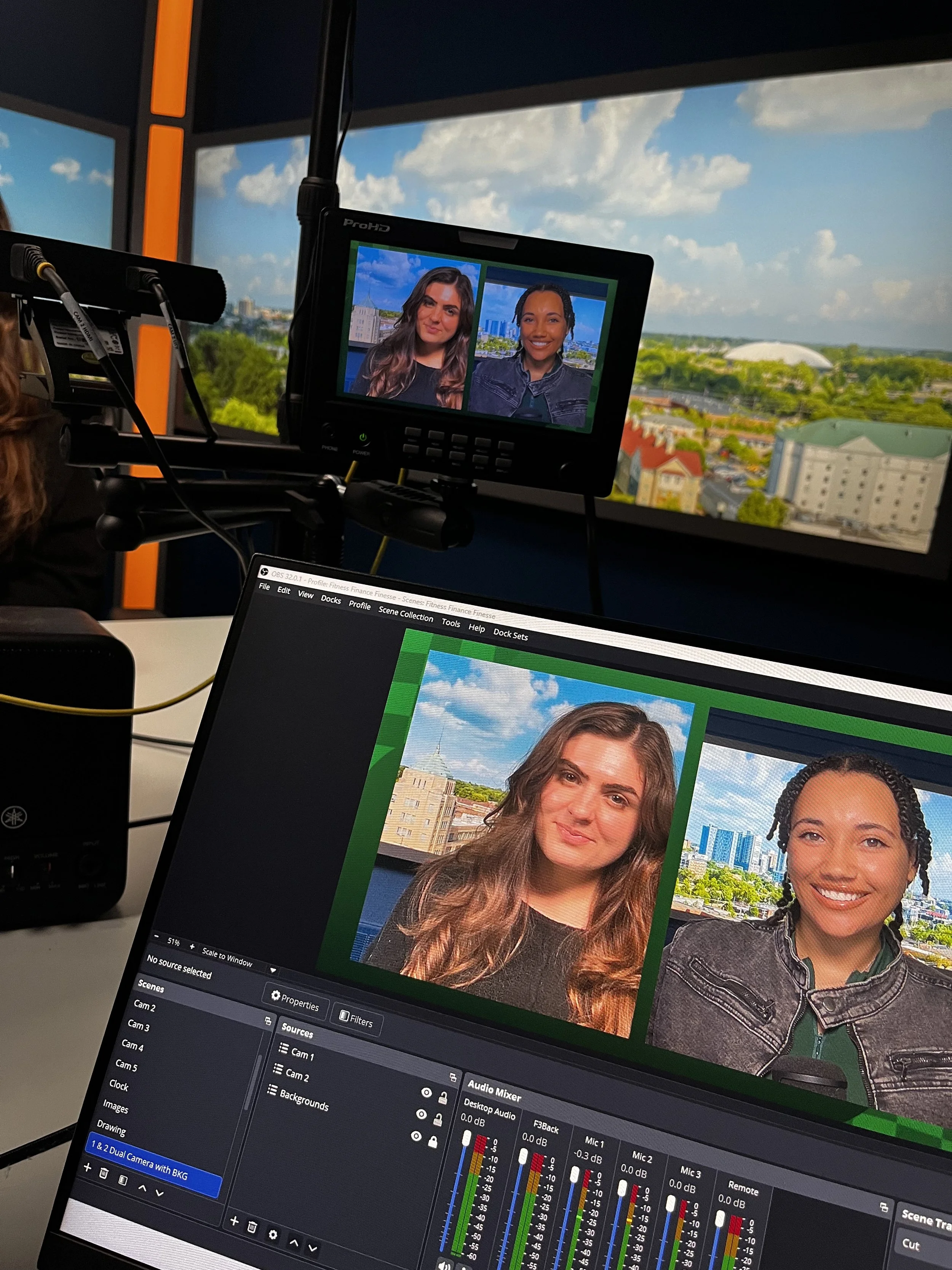  Close-up of Jaelyn Vickery and Grace Ganley smiling together behind a podcast desk at WCIA, featuring a blue Yeti travel mug that reads 'Let's Get Down to Business.' 