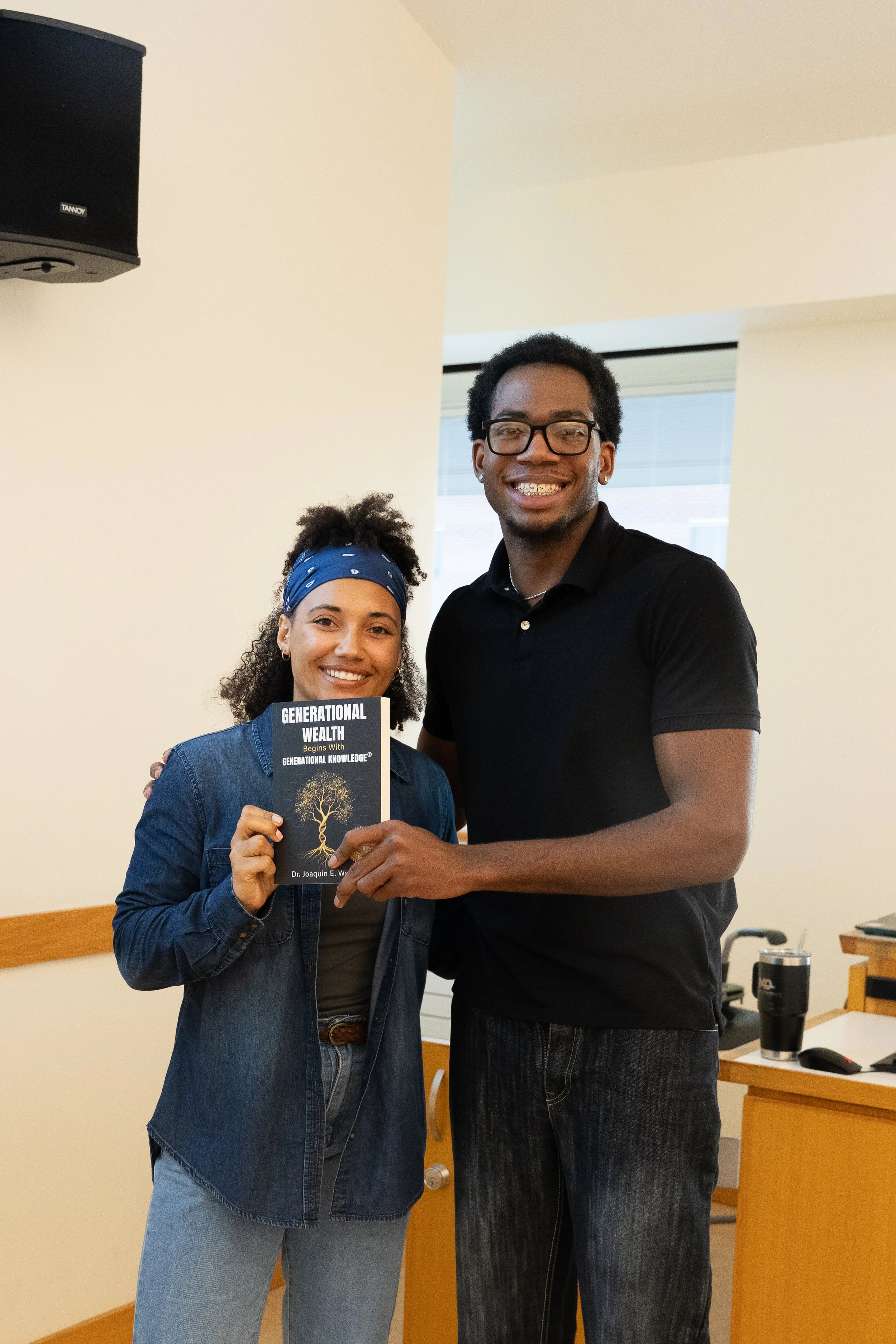 Two smiling students at Gies College of Business holding a copy of the book "Generational Wealth" by Dr. Joaquin E. Wallace during a financial literacy event.