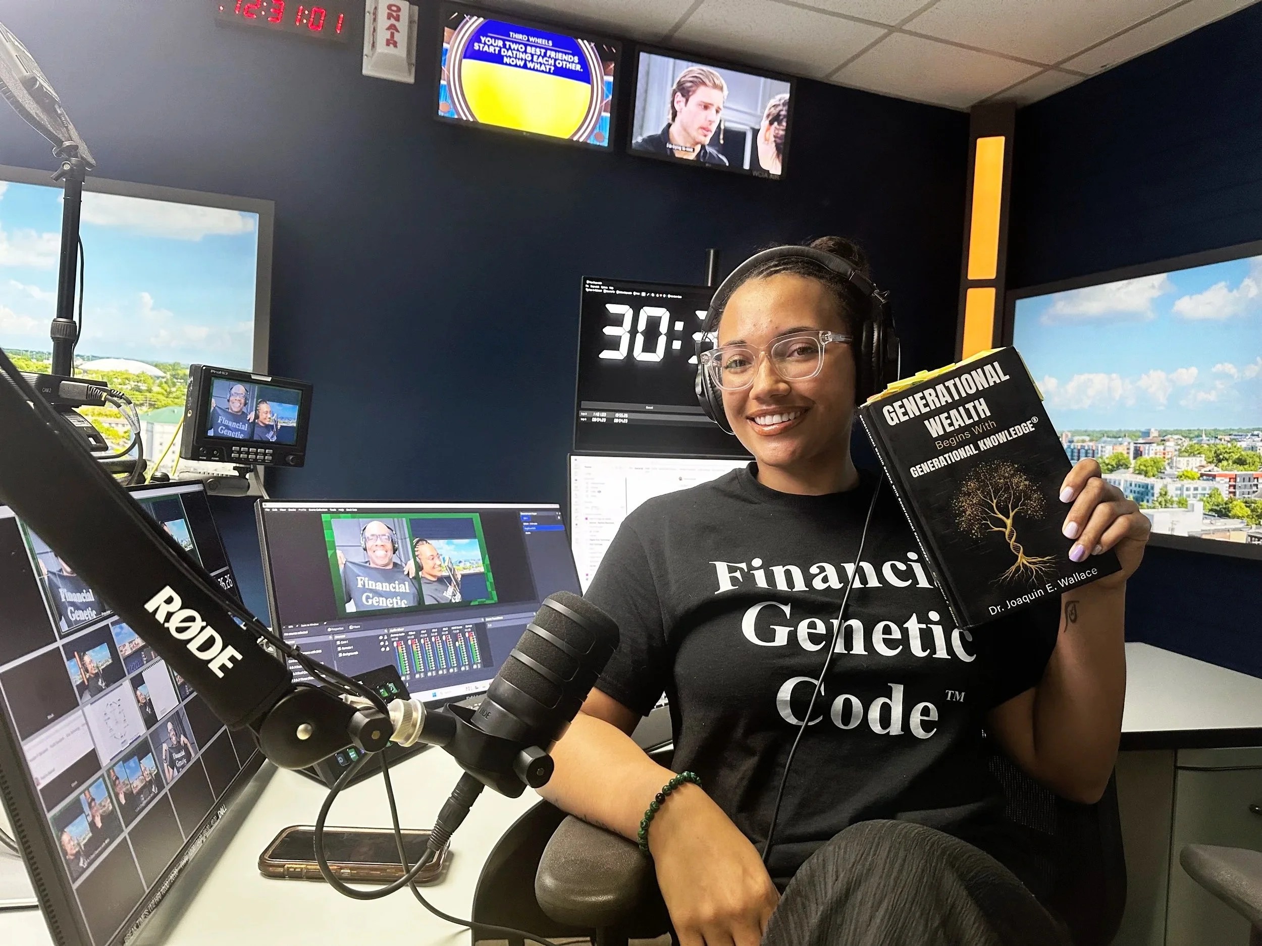 F3 podcast host JaeVic smiling in a recording studio while holding up Dr. Joaquin Wallace's book "Generational Wealth Begins With Generational Knowledge" and wearing a black Financial Genetic Code t-shirt.