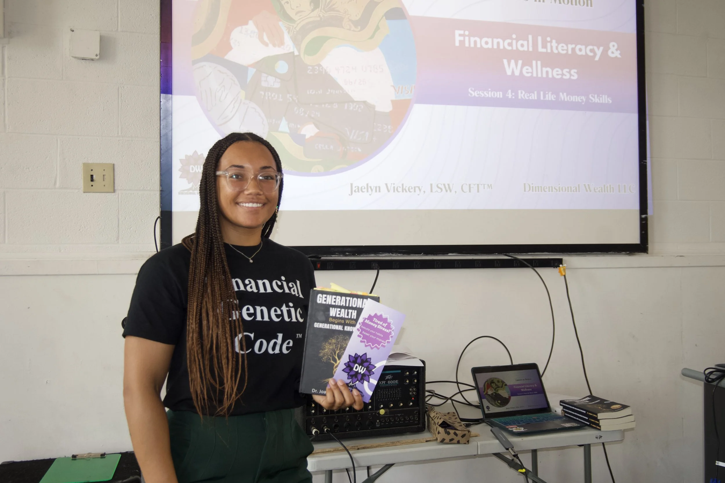 Jaelyn Vickery holding copies of Generational Wealth and Dimensional Wealth pamphlets in front of a financial literacy and financial wellnesspresentation slide.