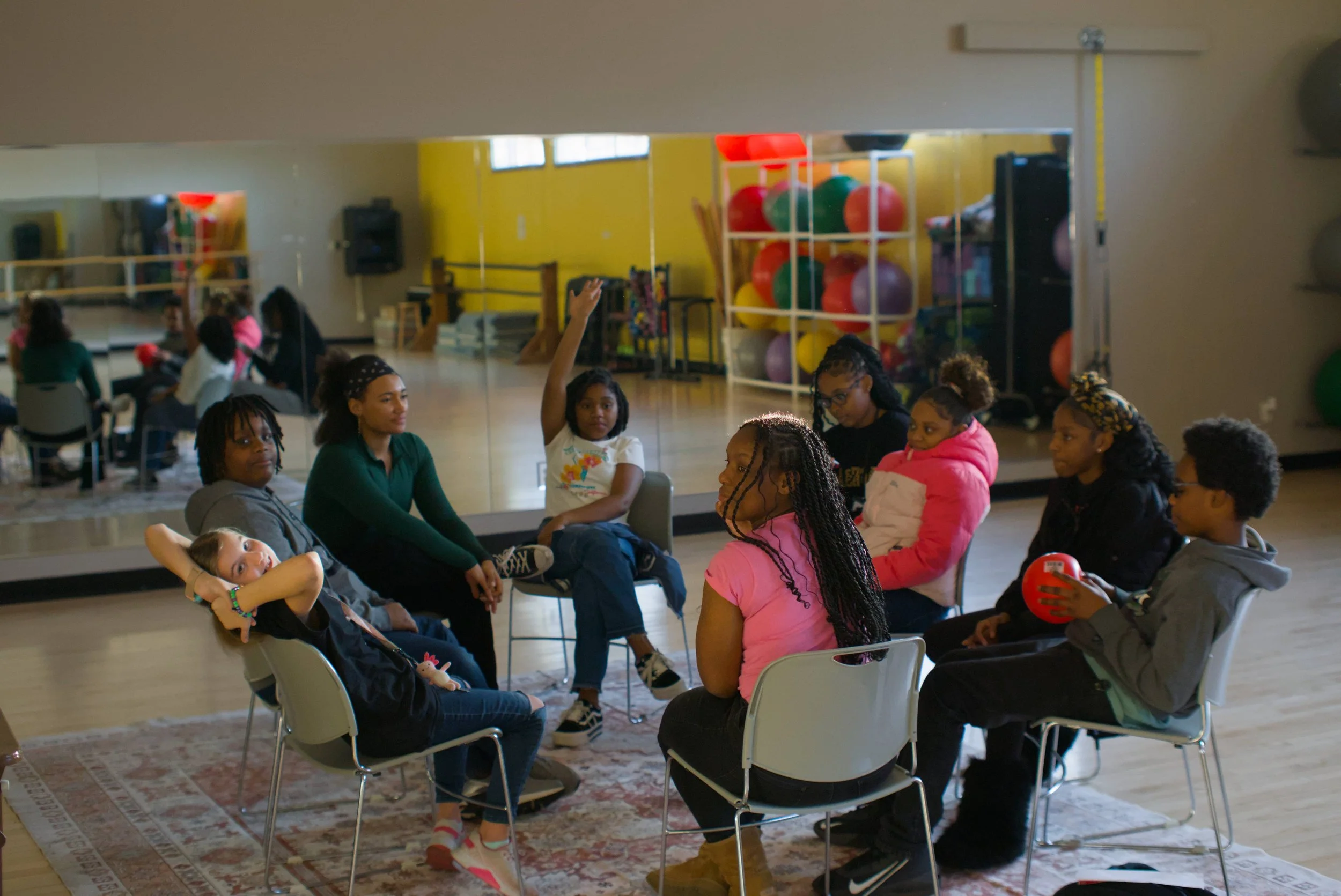 Woman sitting in a circle with teenagers holding a red ball speaking with the participants about financial literacy and wellness.