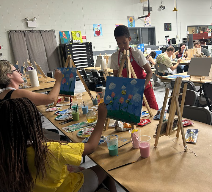 Children painting on small canvases at a classroom art table with paints and brushes.