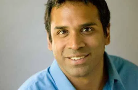 Smiling man wearing a blue shirt in front of a neutral background.