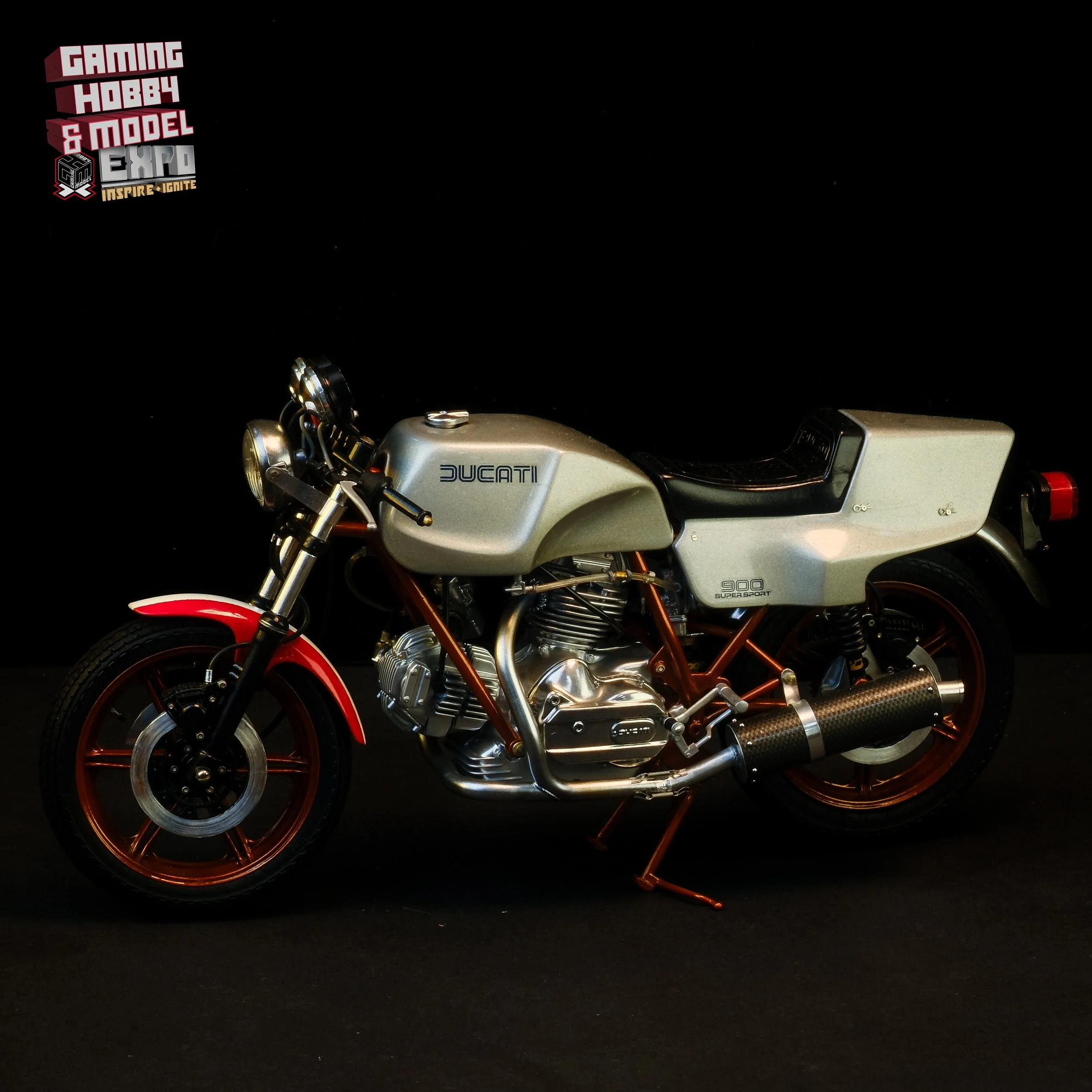 A silver Ducati 900 Super Sport motorcycle with red accents and black seat, displayed against a black background at an expo.