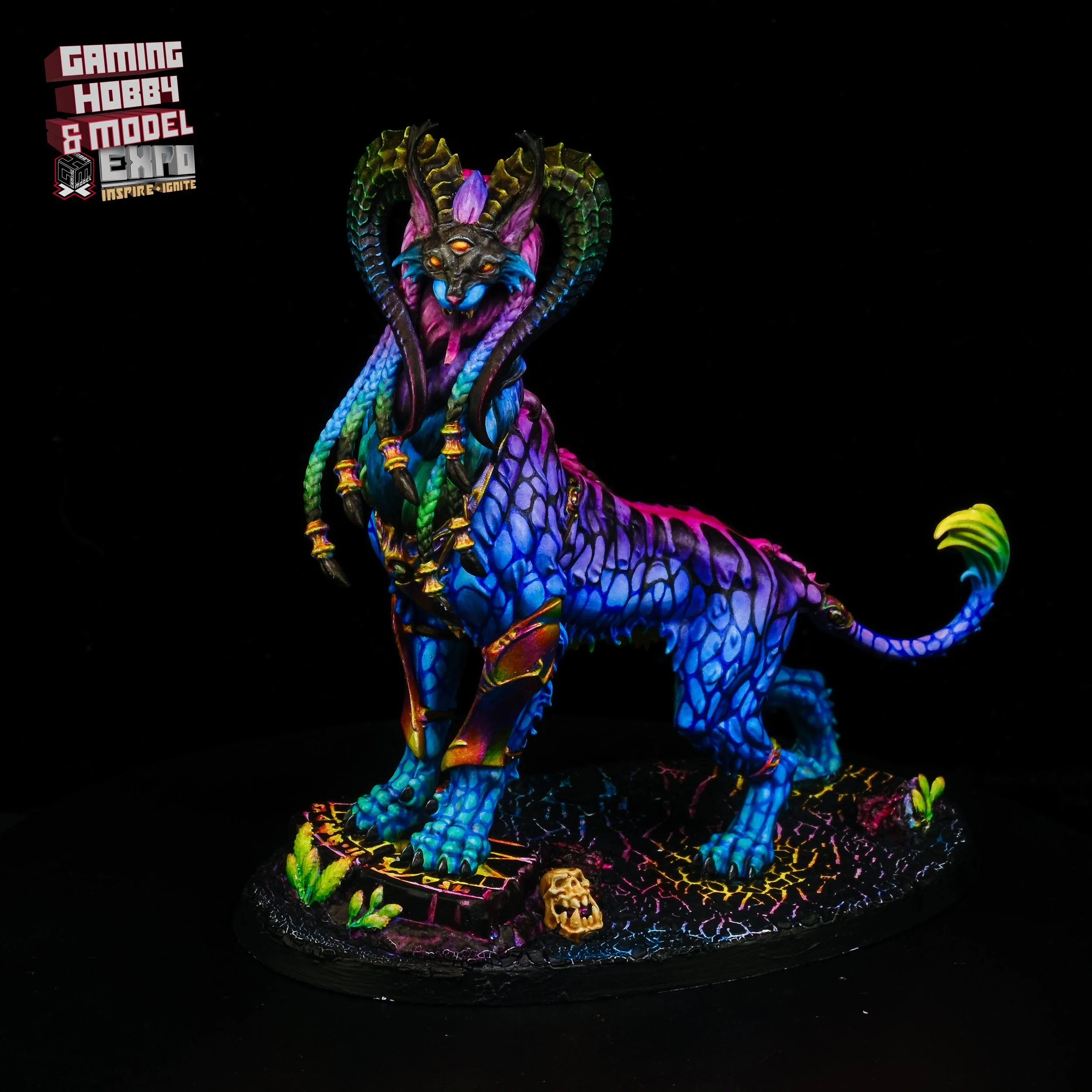 Colorful, painted unicorn with demonic features, horns, glowing eyes, and dragon-like scales, standing on a detailed base with small skulls and plants.