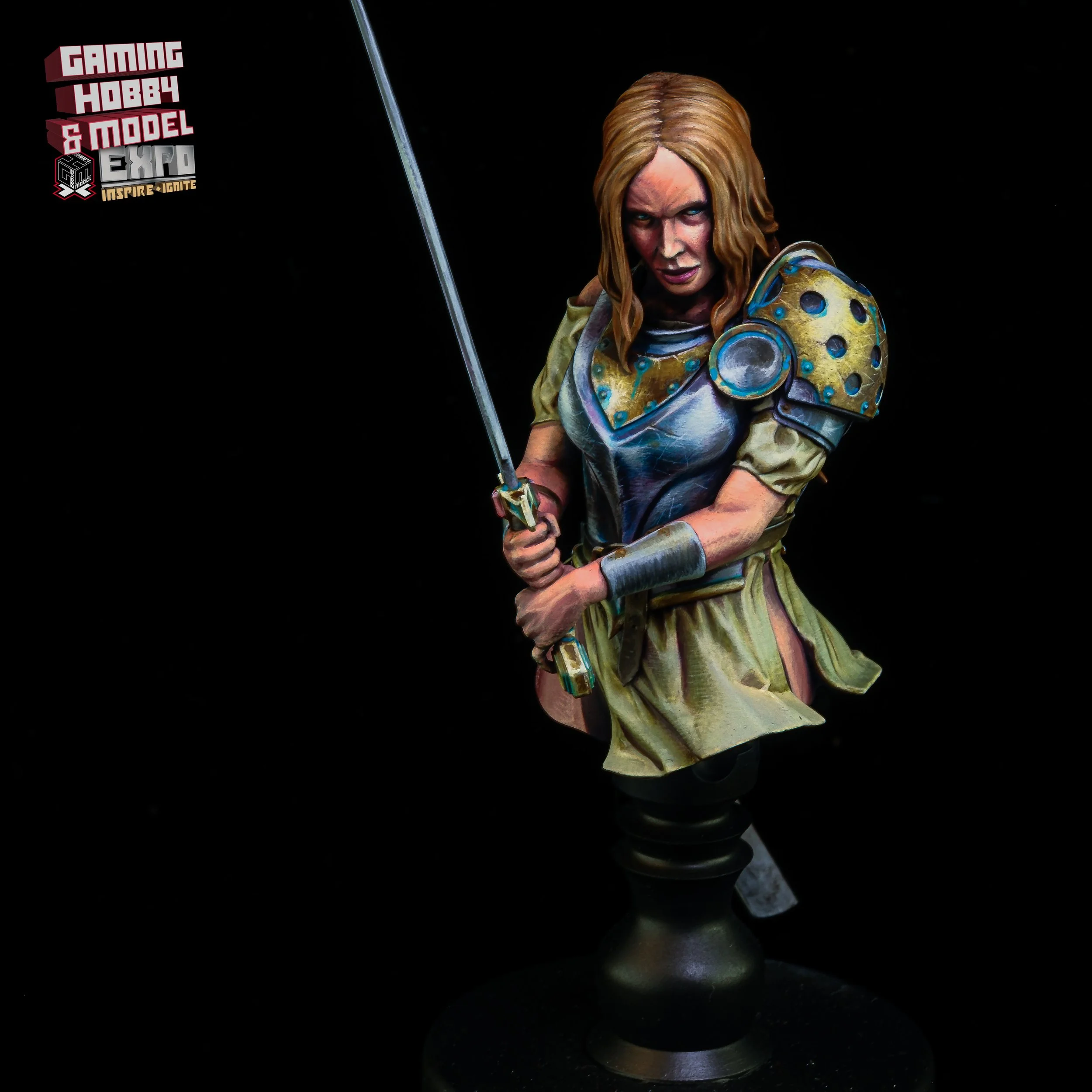 A painted miniature figurine of a woman in armor, holding a sword, with shoulder armor, a skirt, and long, wavy hair, displayed against a black background.