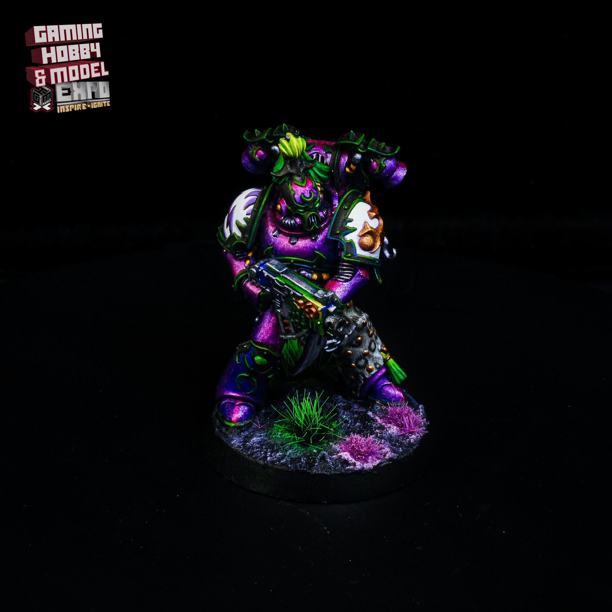 A brightly colored miniature or model figurine of an orc warrior wielding a gun, standing on a round base decorated with grass and pink flowers, with black background and in neon colors.