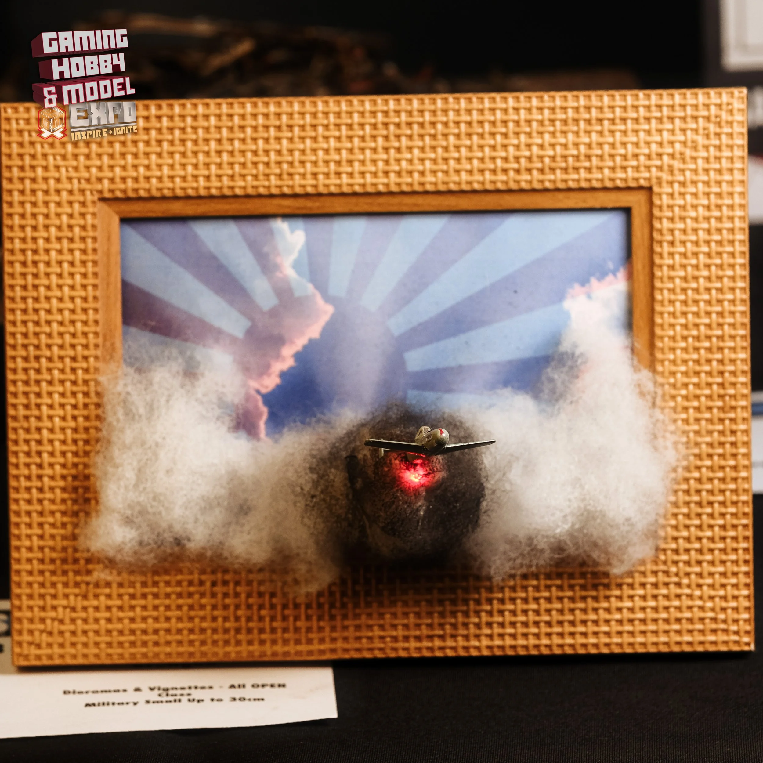 Model airplane taking off through clouds on a diorama with a framed background and radiation warning sticker in the top left corner.