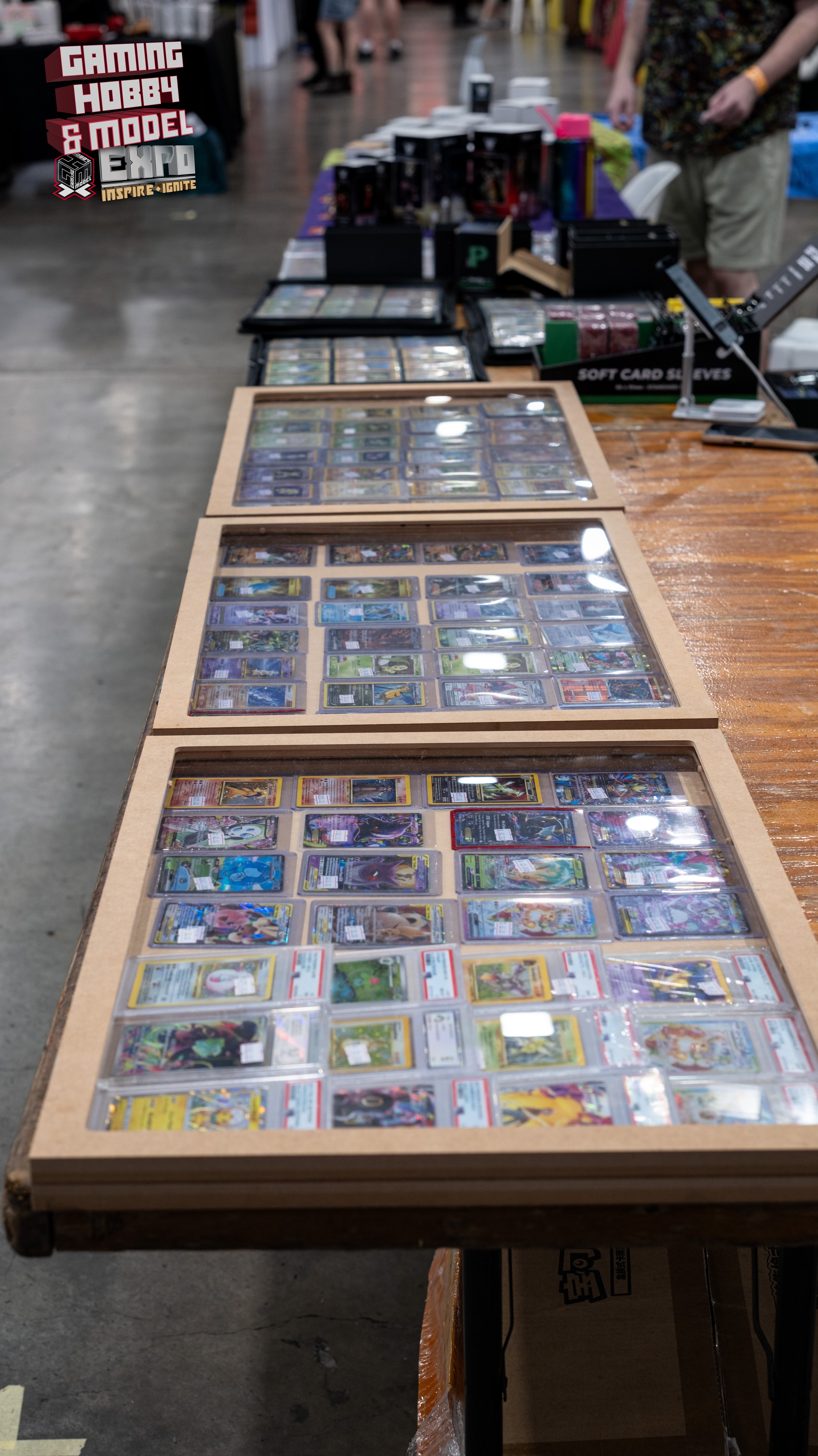 Table displaying various collectible trading cards in plastic cases at a gaming convention.