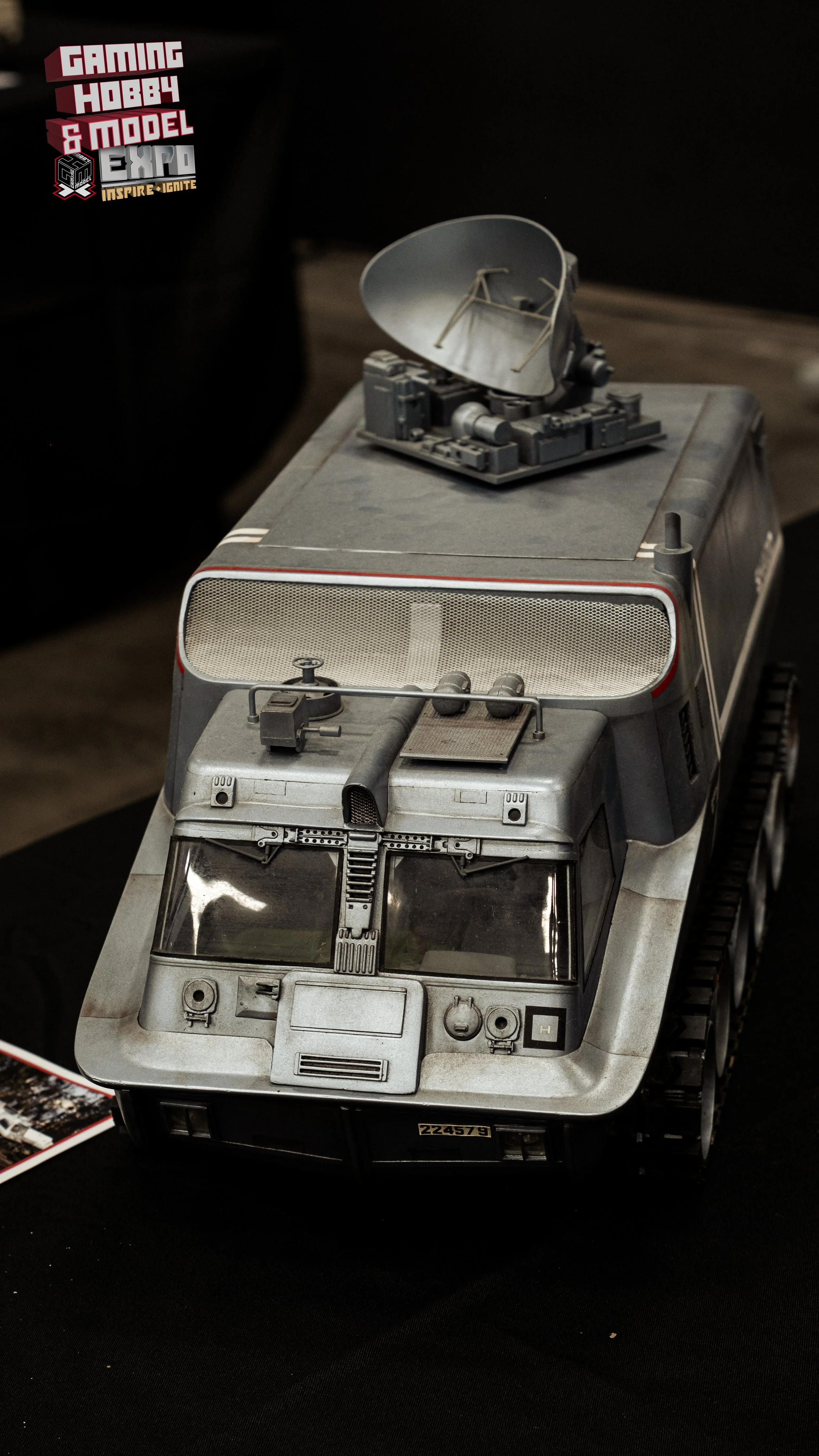 Model of a military vehicle with mounted equipment, displayed on a black surface at a convention.