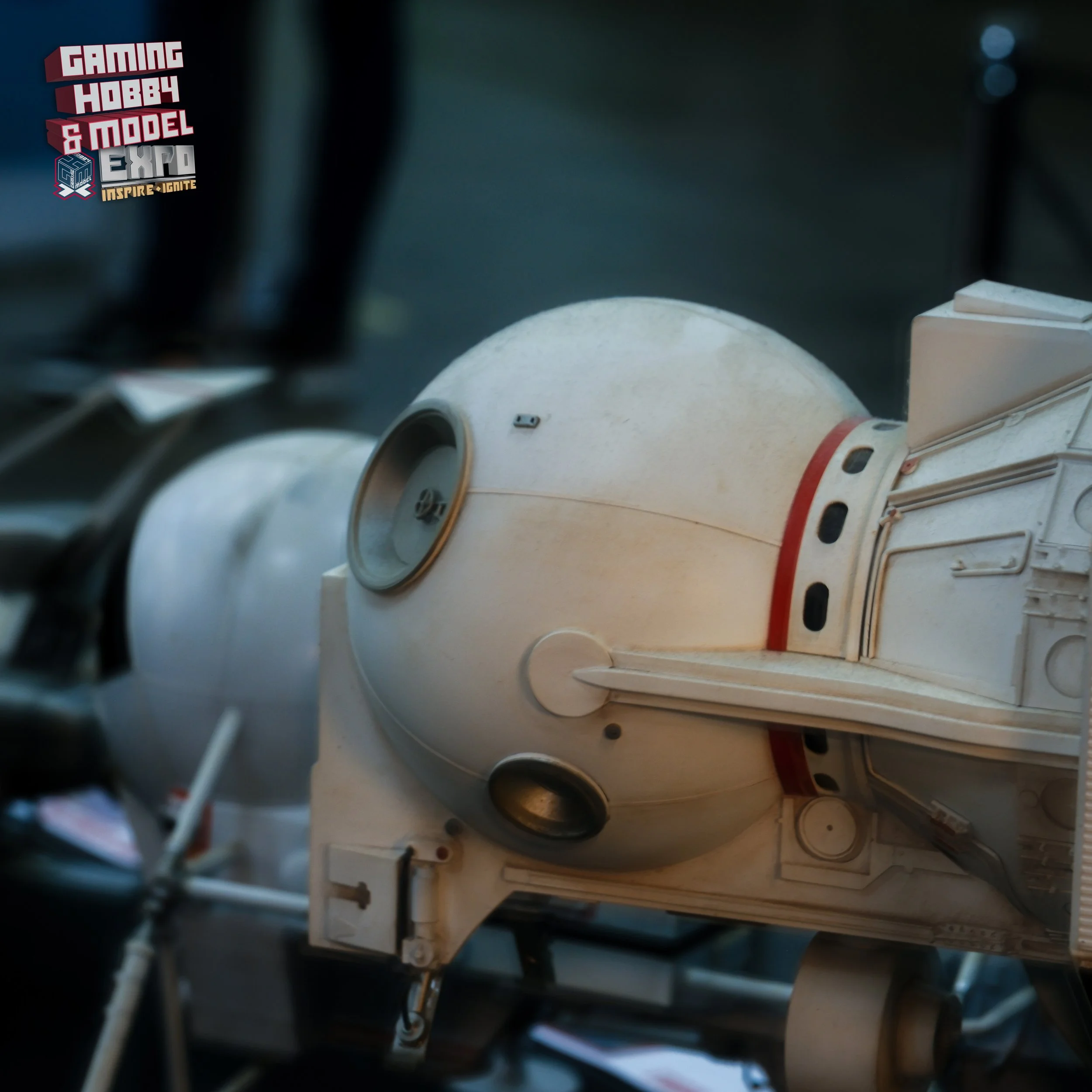 Close-up of a replica of the HAL 9000 spaceship from 2001: A Space Odyssey, sitting inside a museum or exhibit, with a logo in the top left corner reading 'Gaming Hobby & Model Expo.'