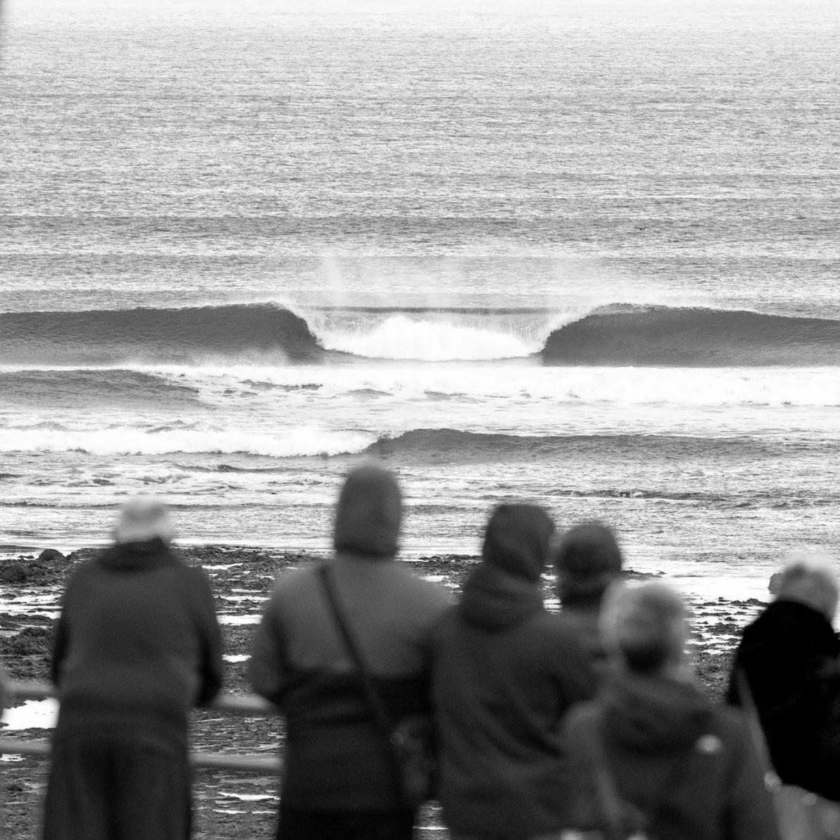 A group of people watching waves at the beach, with some waves breaking in the distance.