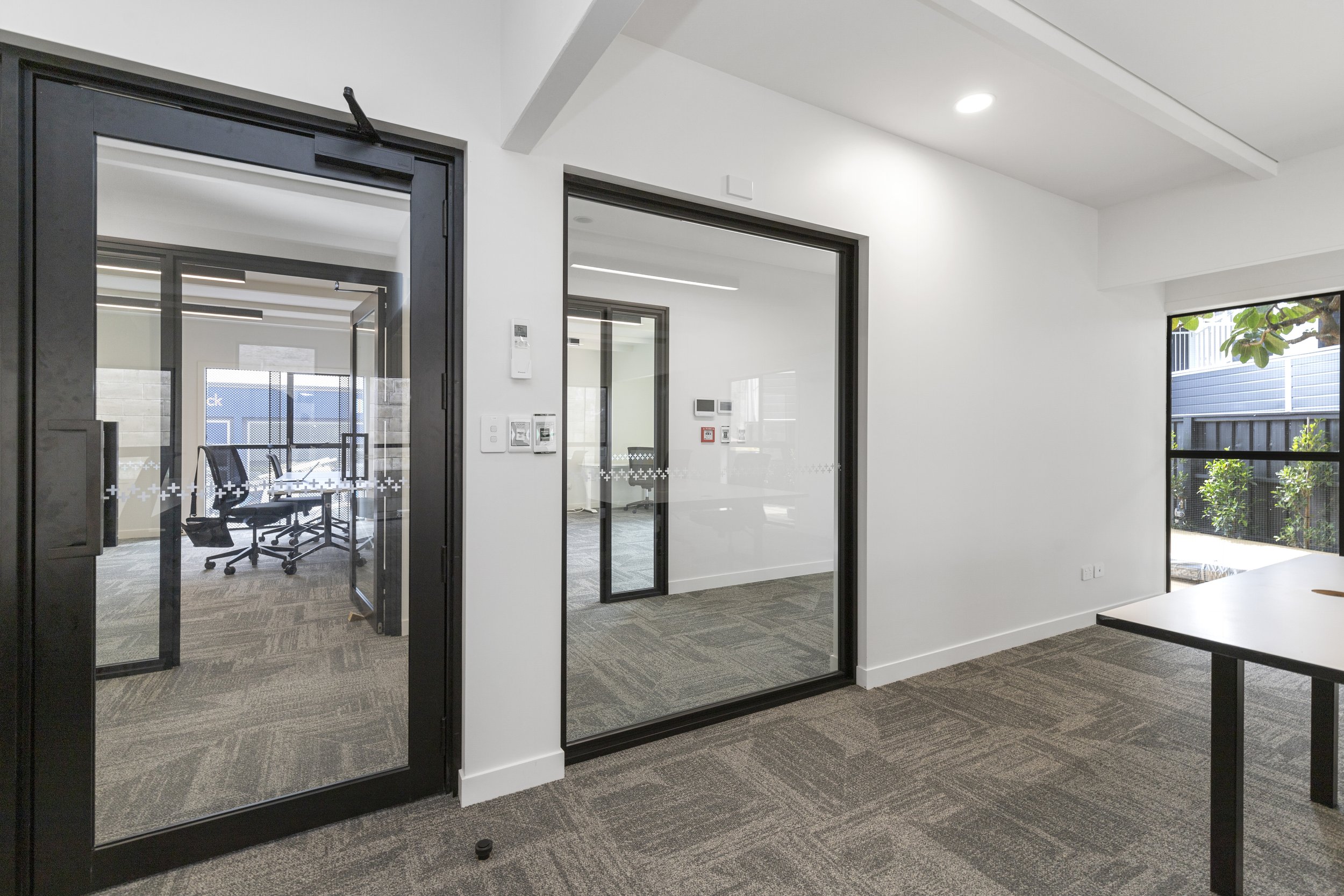 Modern office interior with glass doors and conference room, featuring carpeted floors and sleek furniture.