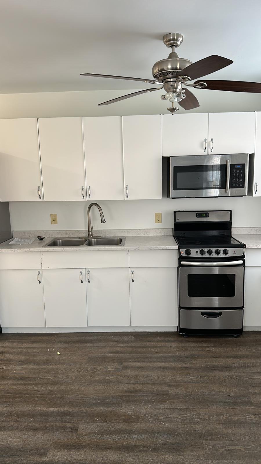 Modern kitchen with wooden flooring, white island bench, wooden bar stools, pendant lights, and built-in oven.