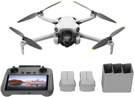 A white quadcopter drone with four propellers, a remote control with a display, two gray chairs, and a black container with four compartments.
