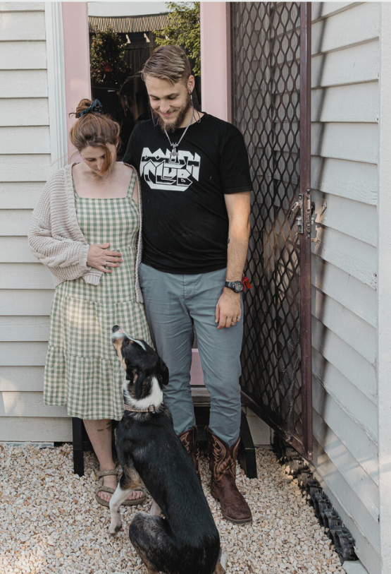 Couple and dog standing outside a house with a white facade.