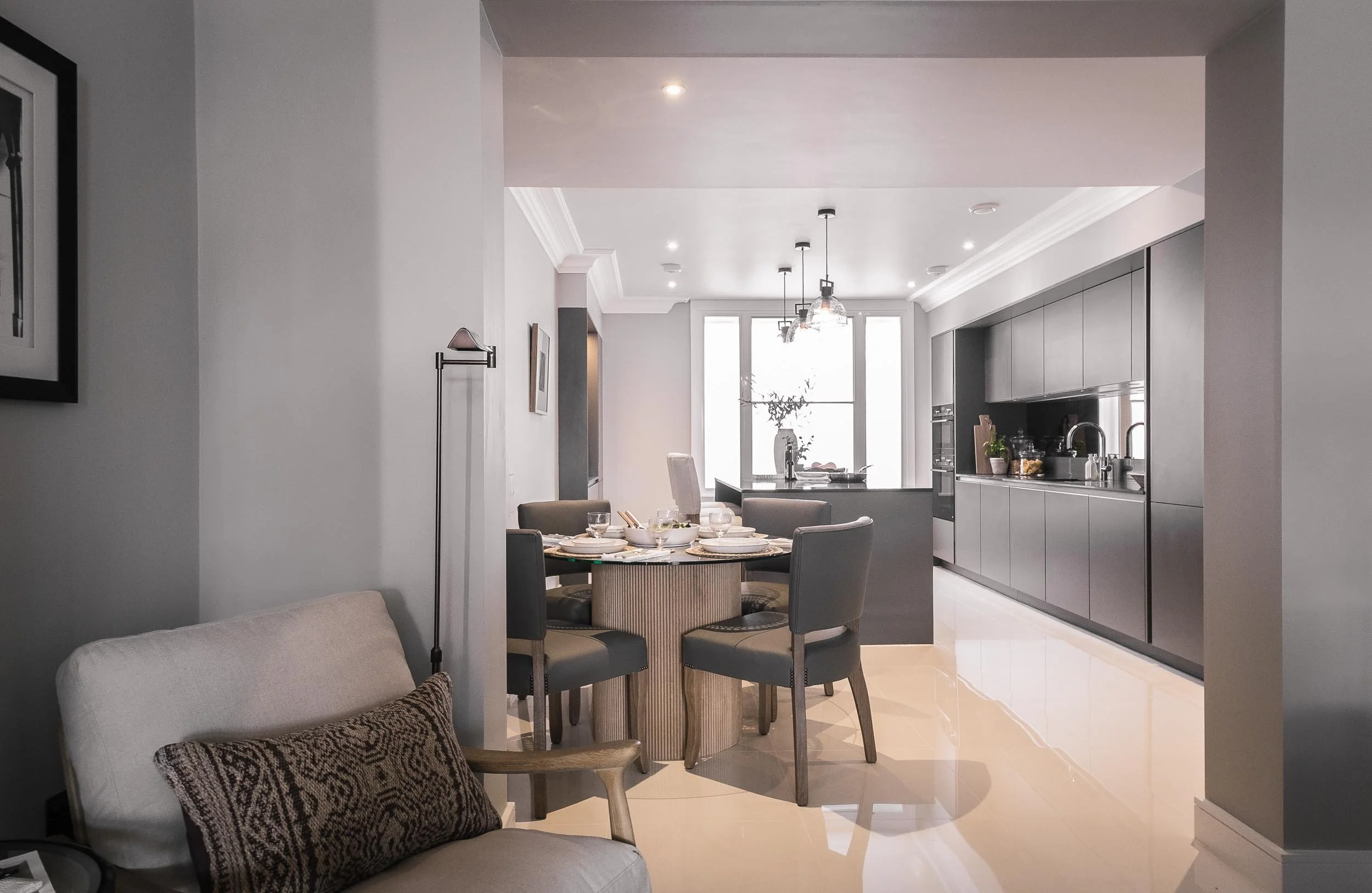 Modern open-concept living and dining area with gray and neutral decor, round dining table set with white dishes, and a sleek kitchen with black cabinets and large windows.