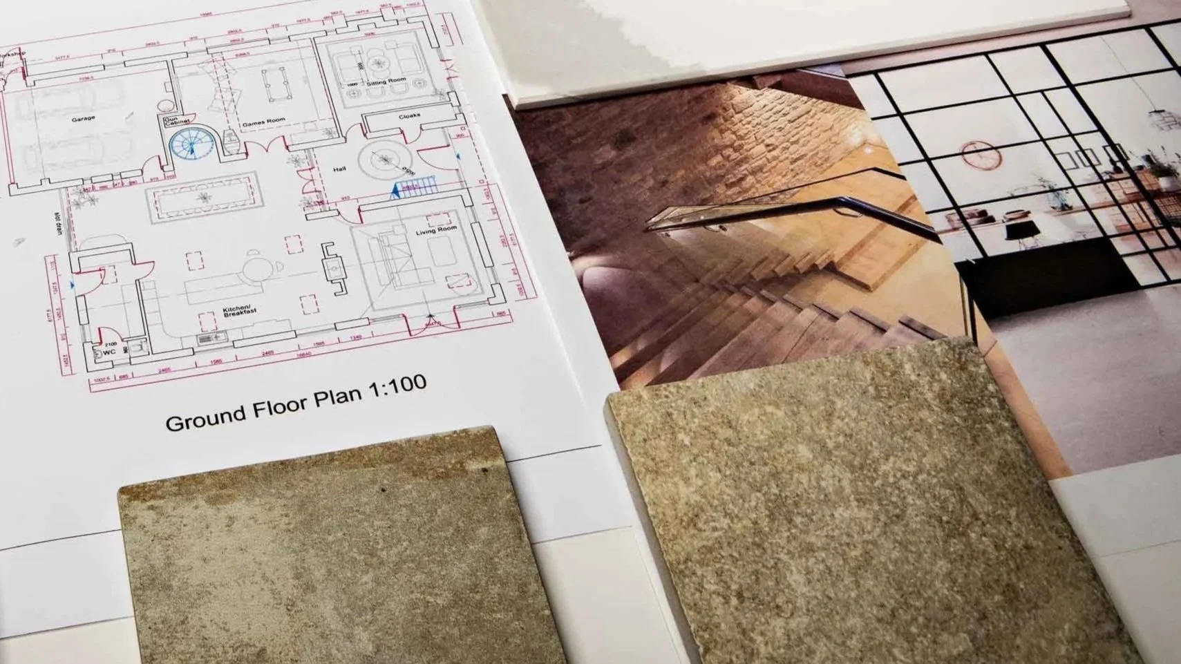 Architectural blueprints, interior design photographs, and samples of flooring and tile materials spread out on a table.