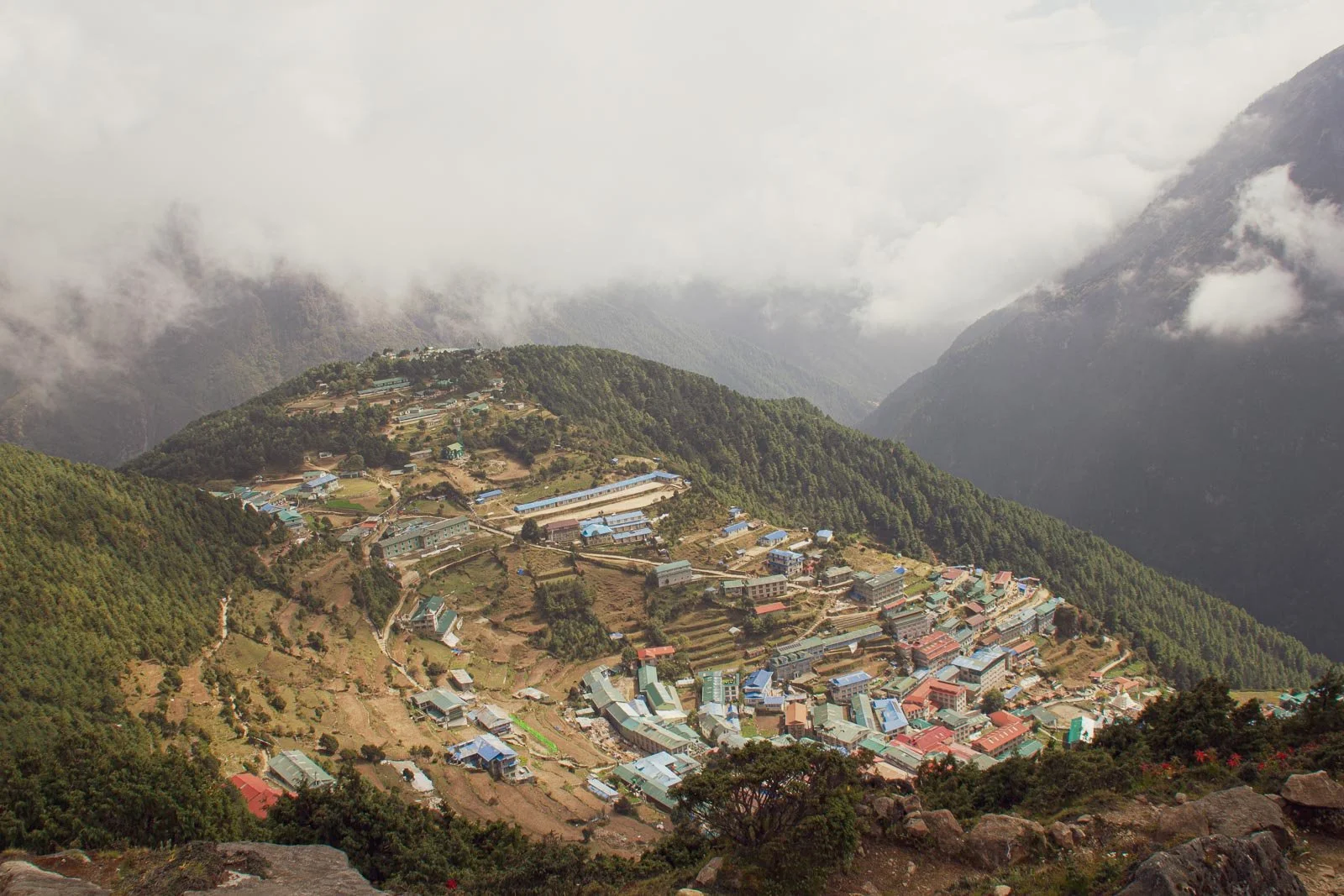  Der Anstieg zum Everest View Hotel offenbart einen grandiosen Blick auf Namche Bazar. Bei dem länglichen Gebäude mit blauem Dach auf der Hochebene handelt es sich um die lokale Schule. Weiter unten befindet sich der lebendige Ortskern.  