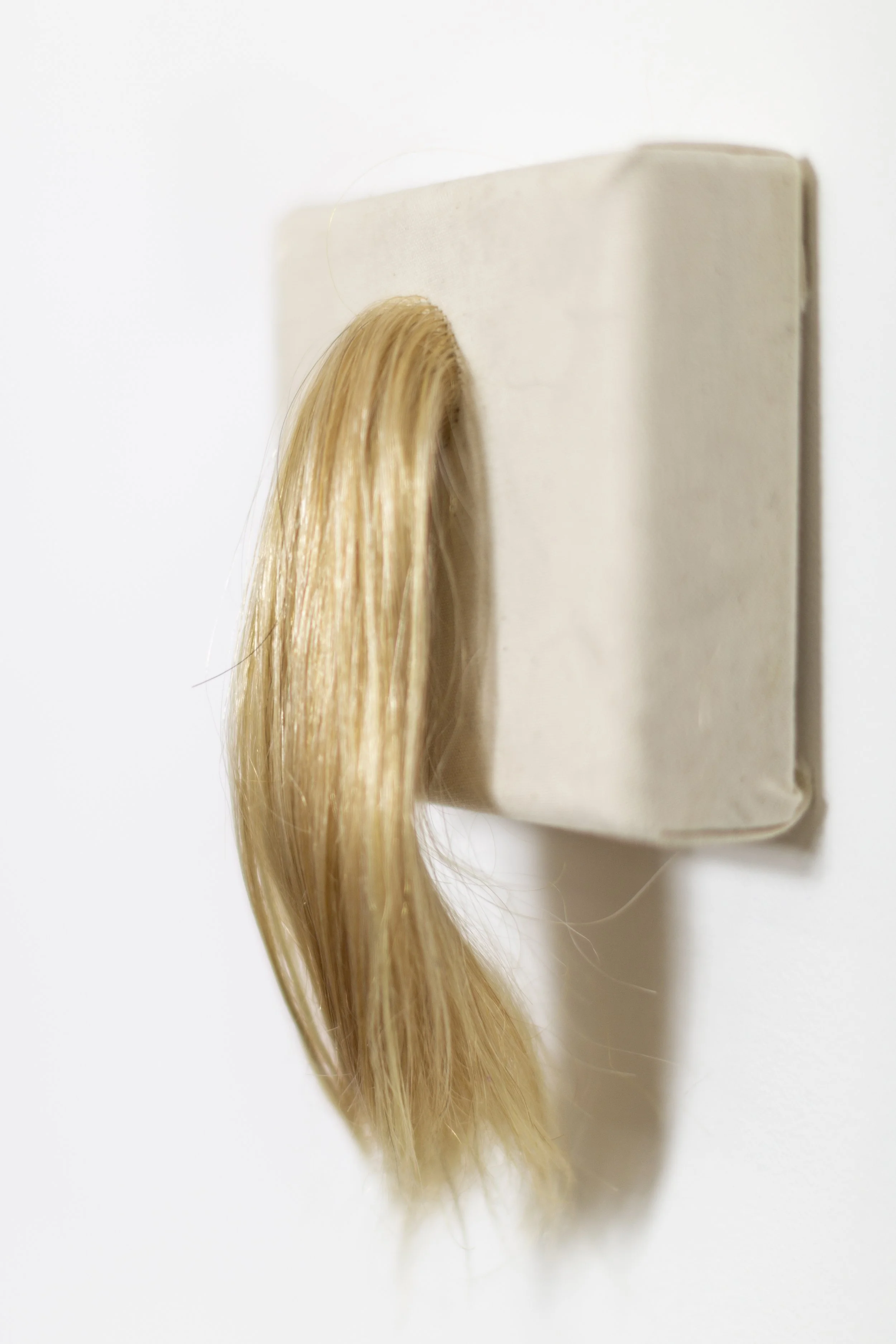 A blonde hair wig hook mounted on a white wall.