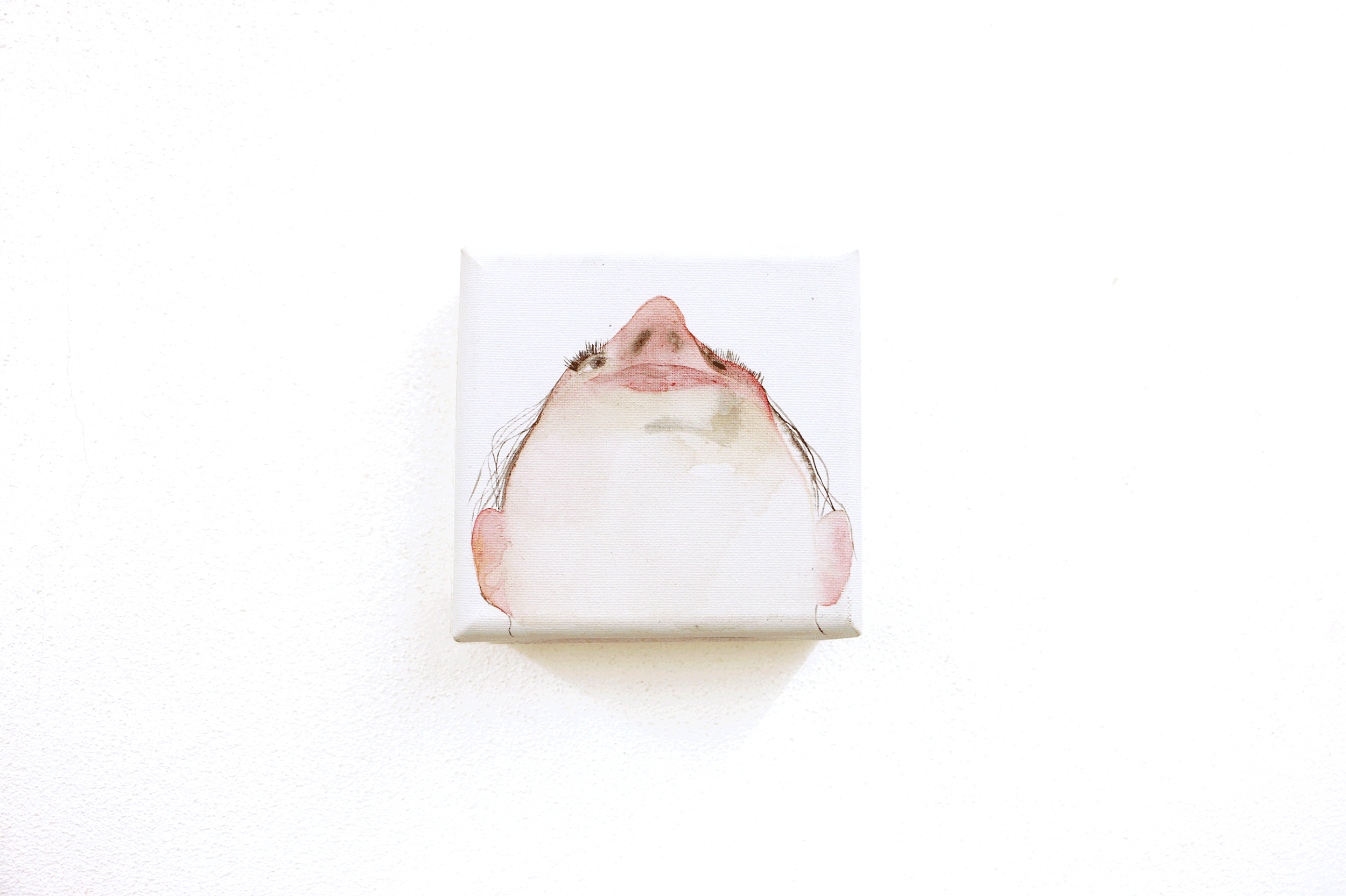 Abstract watercolor painting of an upward-facing face on a small canvas against a white wall.