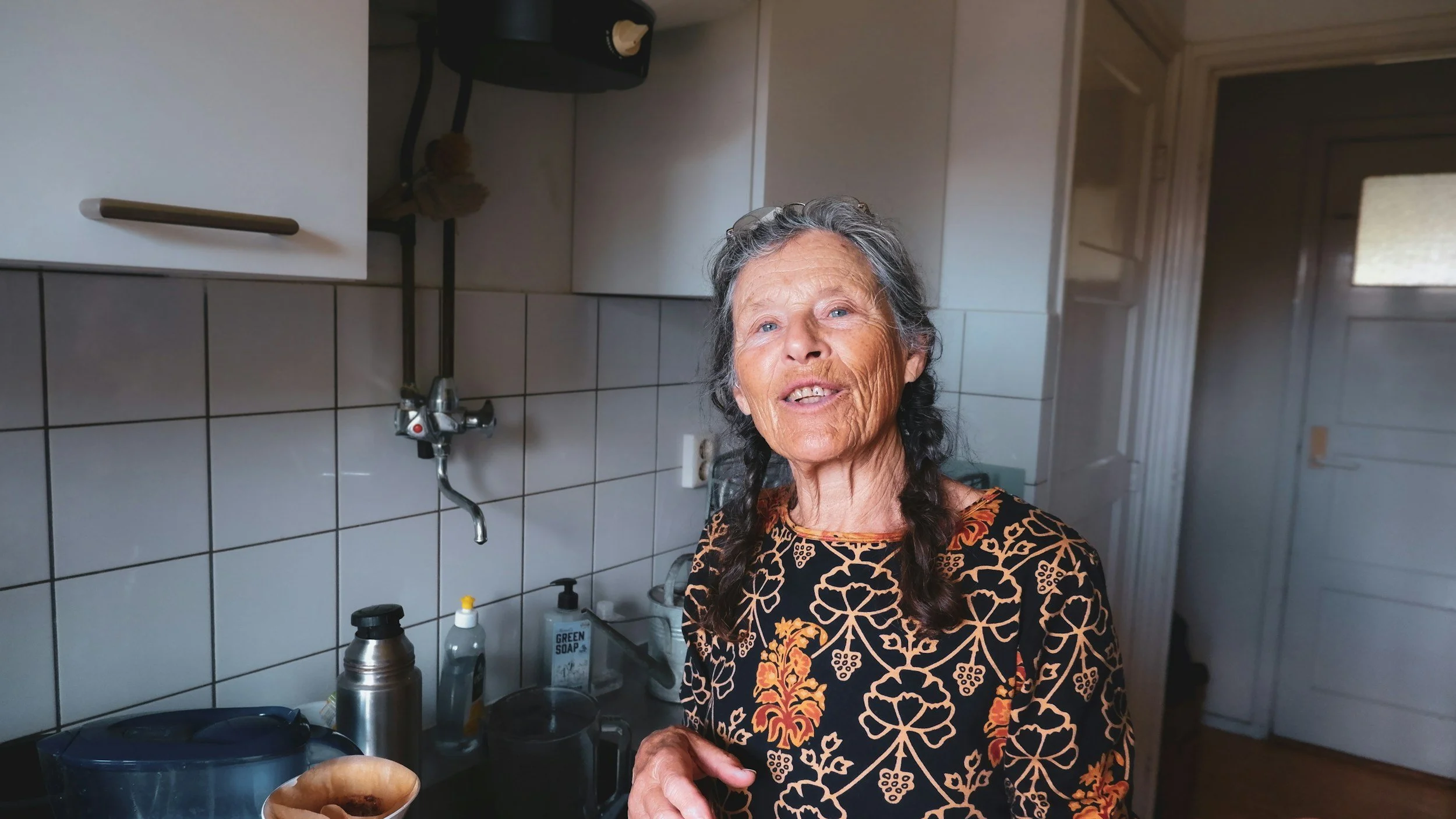 Elderly woman stands in her kitchen smiling