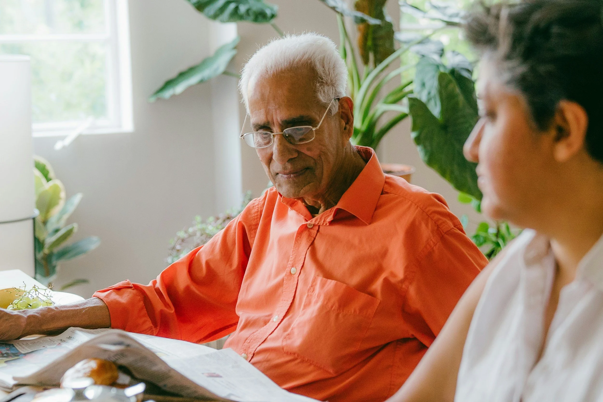 Elderly man in bright orange shirt reads newspaper