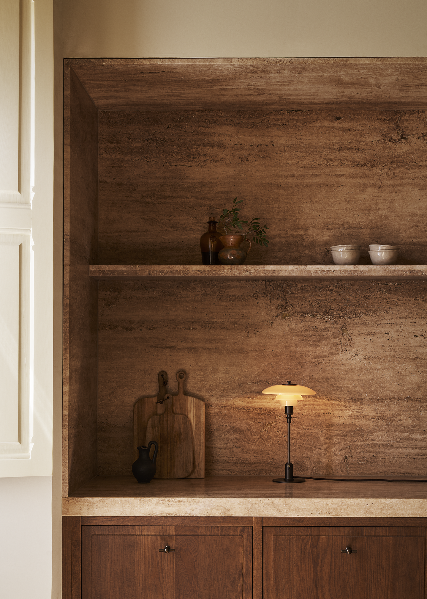 Minimalist kitchen shelf with brown marble and wood cabinets, featuring cutting boards, a PH 2/1 Limited Edition Table Lamp, and ceramic bowls. Staged by Swedish Design Duo DuRietz Design, campaign work for Louis Poulsen.