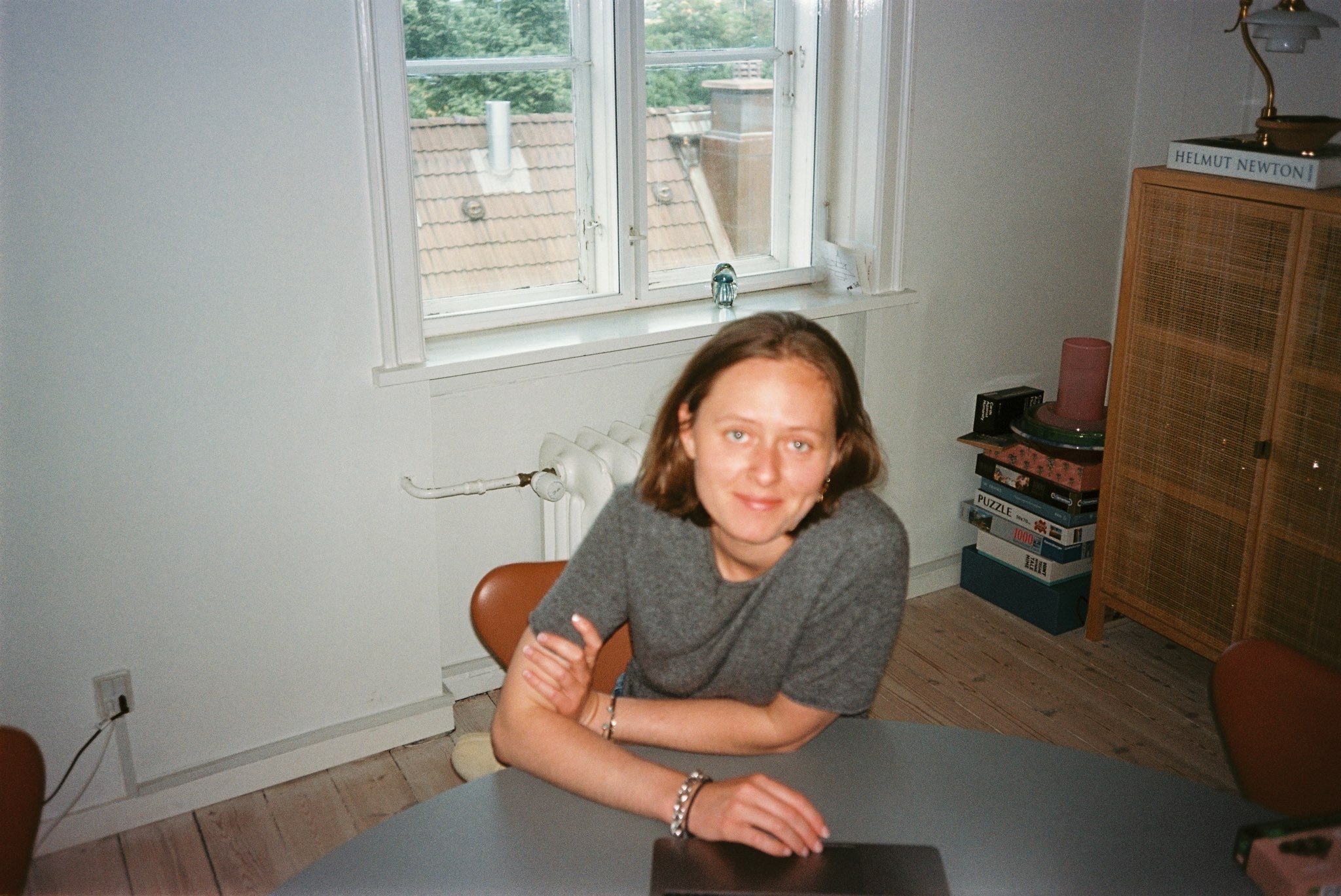 Person leaning on a table in a room with a window, books, and games visible. Thea Raben, Founder of THERA communication.