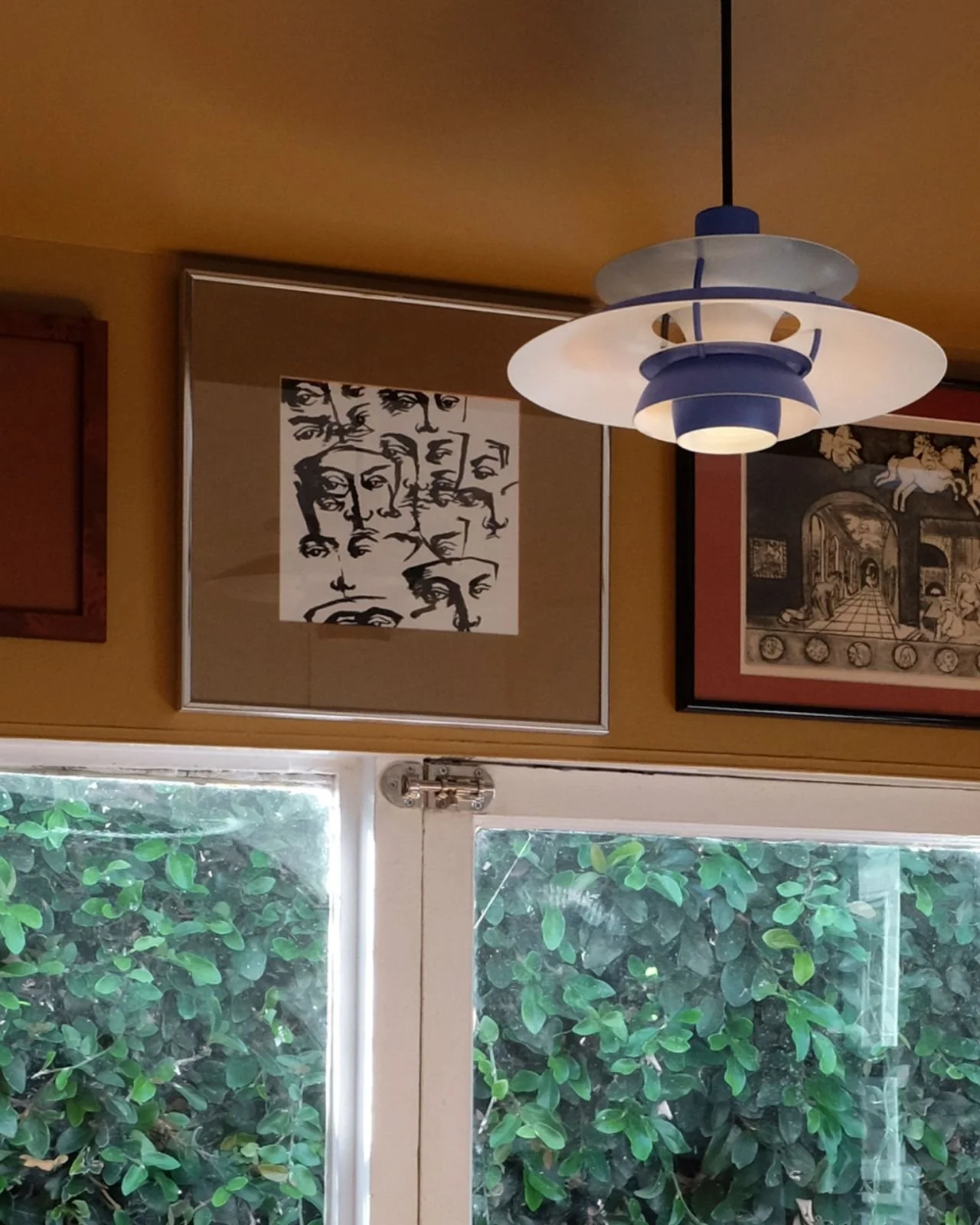 Interior with artwork on wall, PH 5 pendant light, and greenery outside window. Styled by american interior designer Paige Wassel